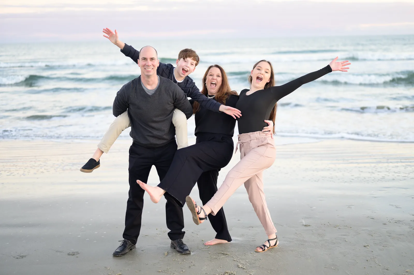 Family of 4 having fun in front of the ocean during winter - Huntington Beach State Park