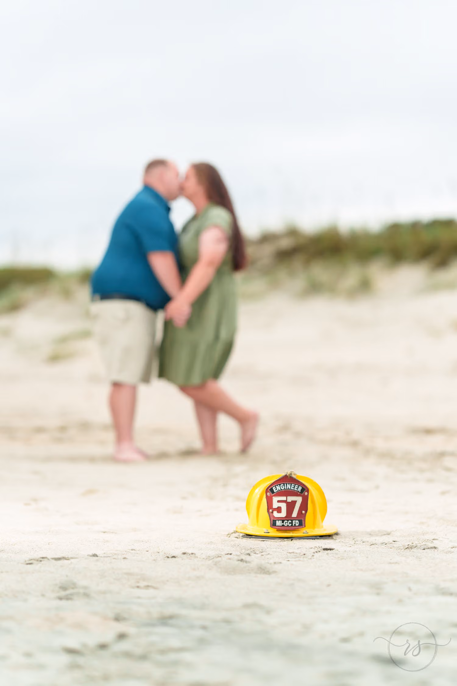 Yellow firefighter helmet in focus on the sand with a couple kissing in the background at Huntington Beach State Park