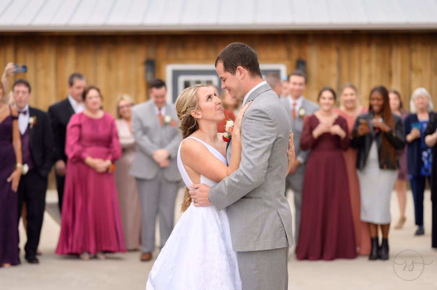 Bride and groom sharing their first dance as smiling family and friends look on at The Blessed Barn