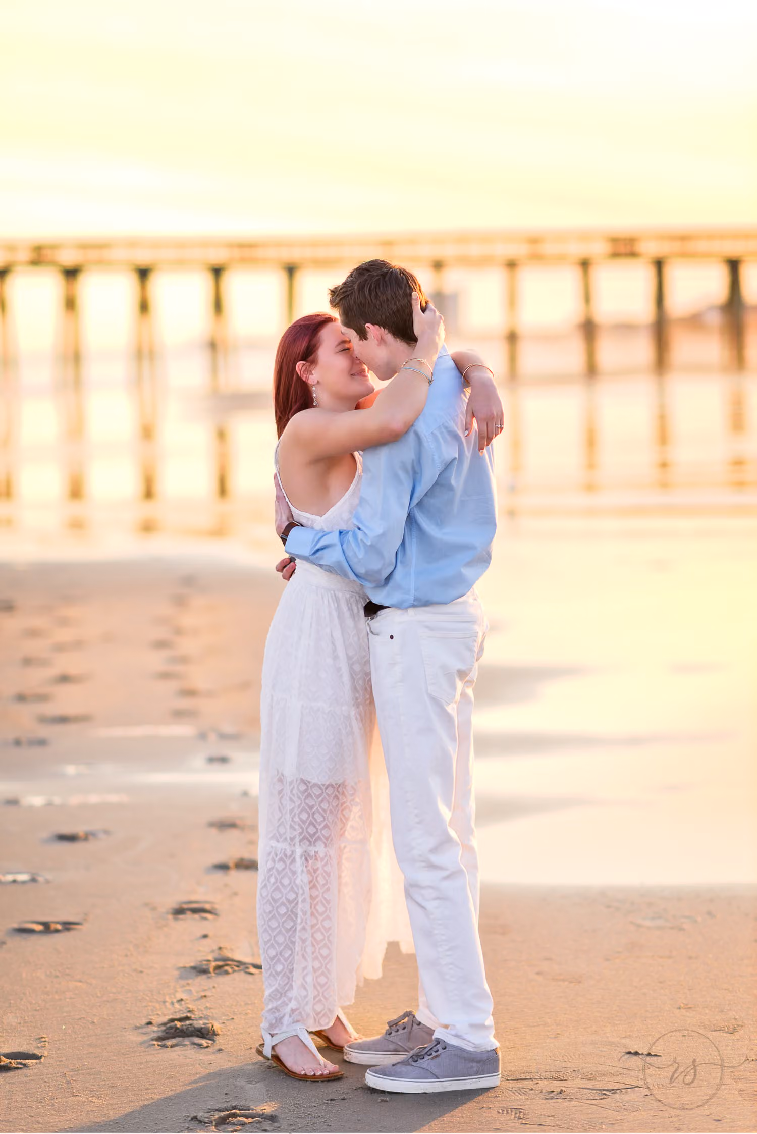 Newly engaged couple hugging and kissing on the sand at golden hour with the pier behind them at Myrtle Beach State Park