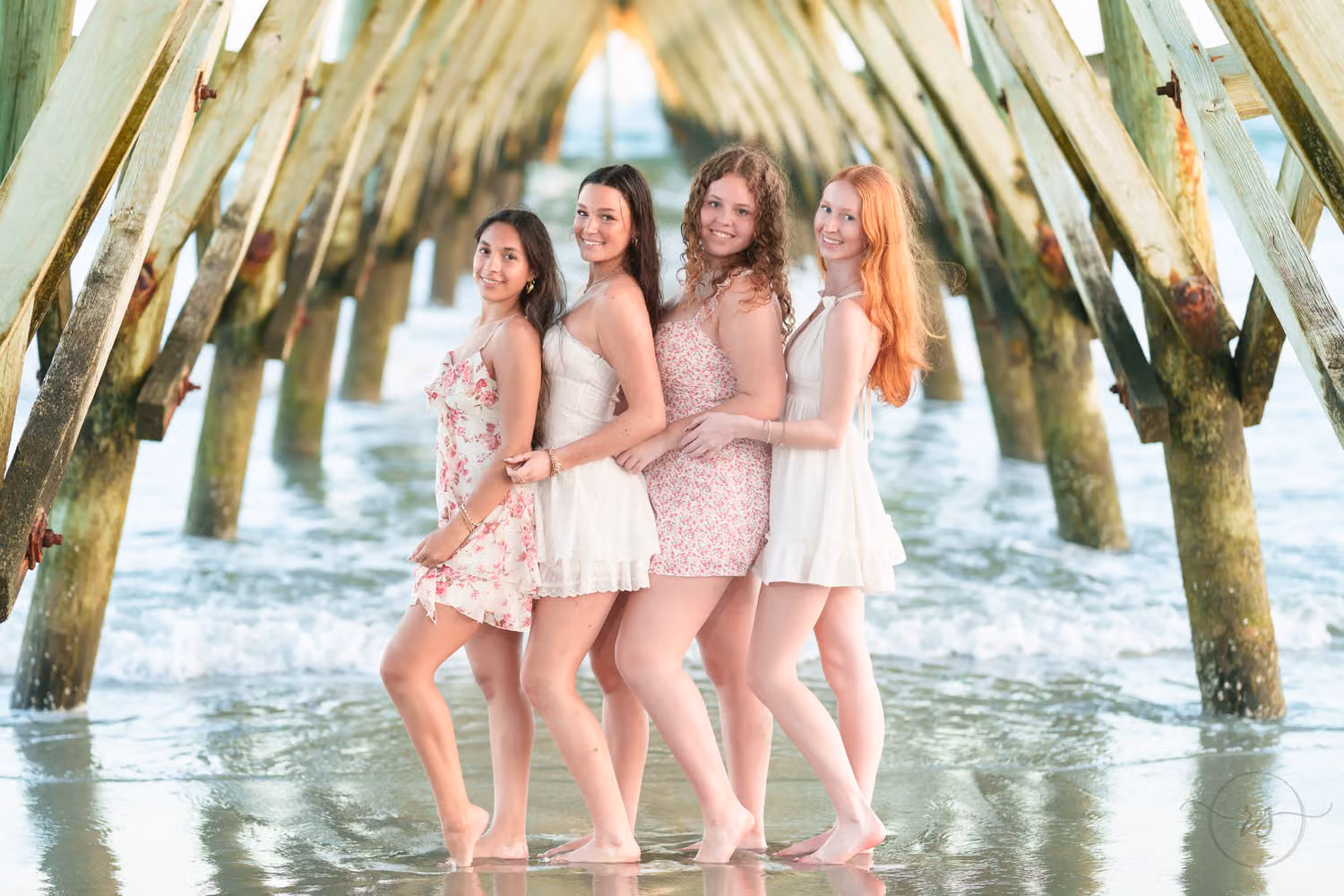 Four senior girls in sundresses standing close together in the shallow water under the pier in North Myrtle Beach