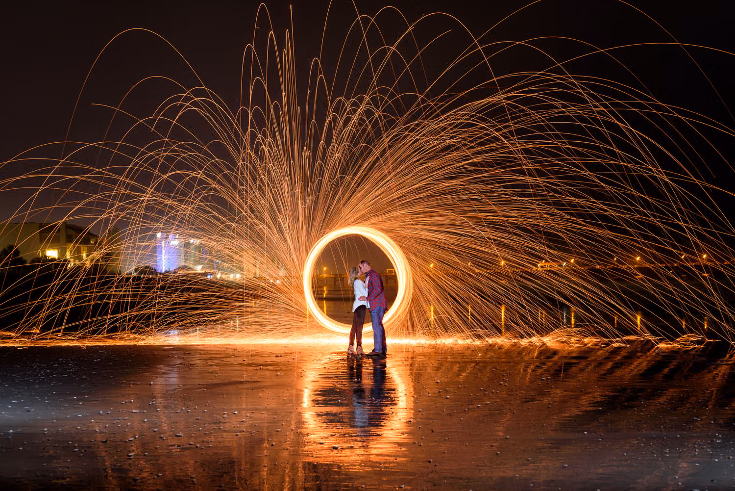 Couple standing inside a spinning ring of sparks from steel wool, reflected on the wet sand at night at Springmaid Beach