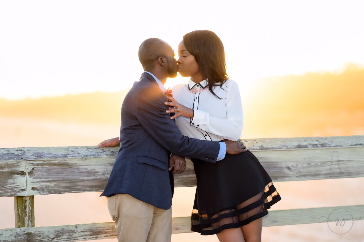 Couple kissing against the pier railing with the golden sunset glowing behind them at Myrtle Beach State Park