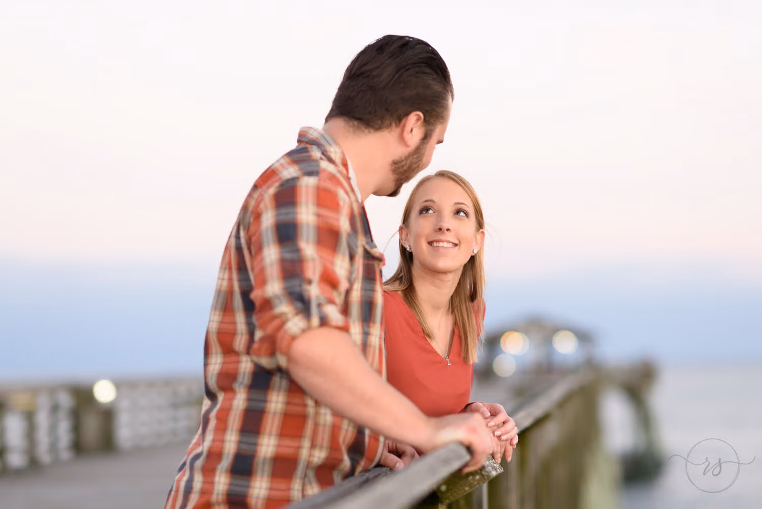 Woman leaning on the pier railing smiling up at her fiancé in a plaid shirt at Myrtle Beach State Park