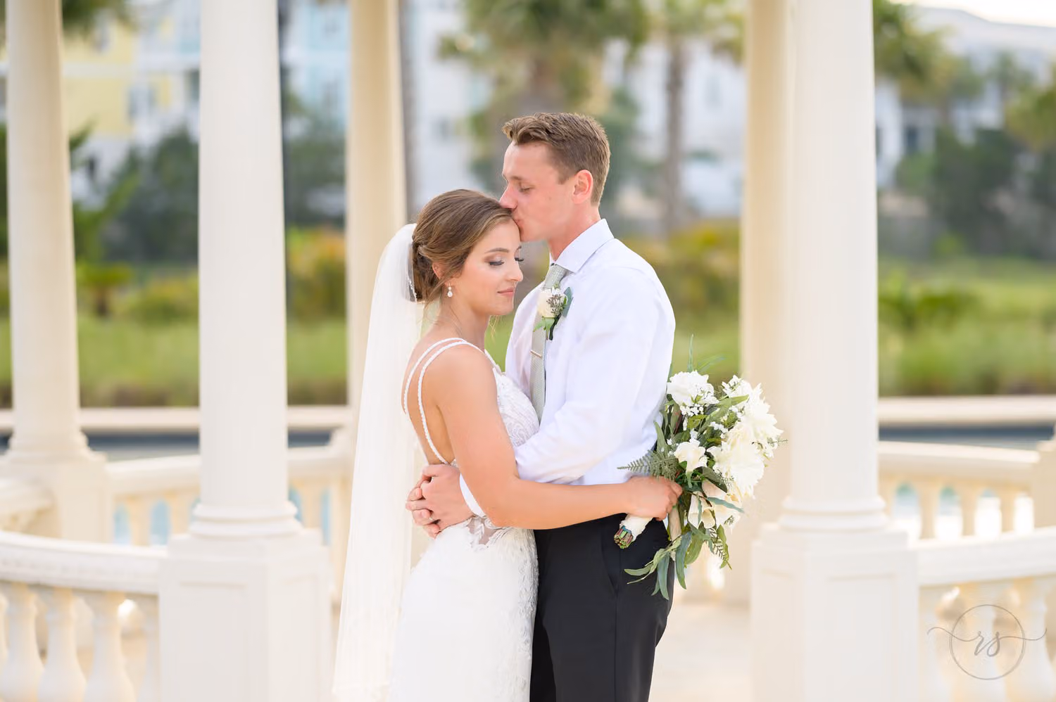 Groom kissing the bride on the forehead as she closes her eyes inside the white gazebo at 21 Main Events
