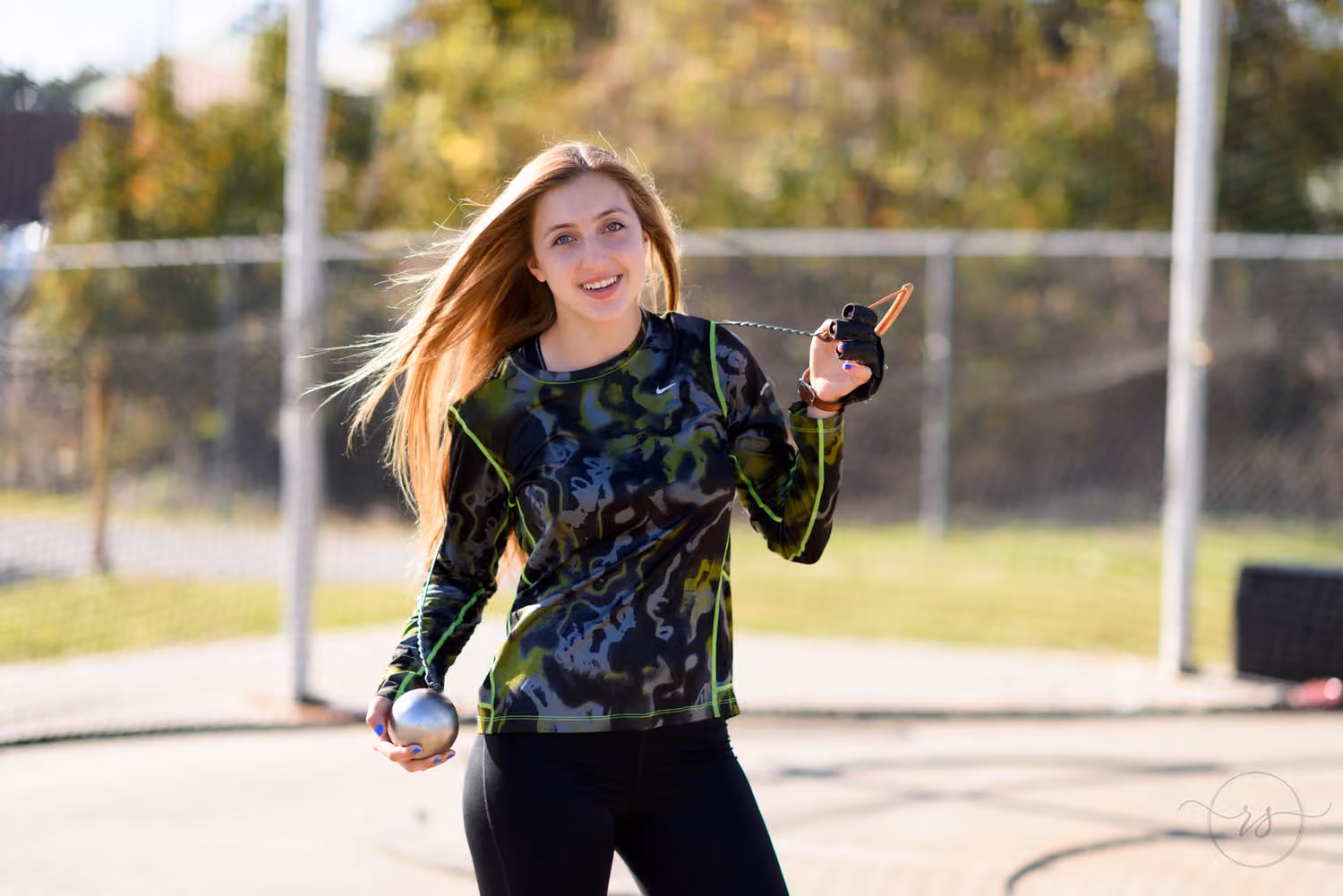 Senior track athlete smiling with her throwing hammer inside the throwing cage at Myrtle Beach High School