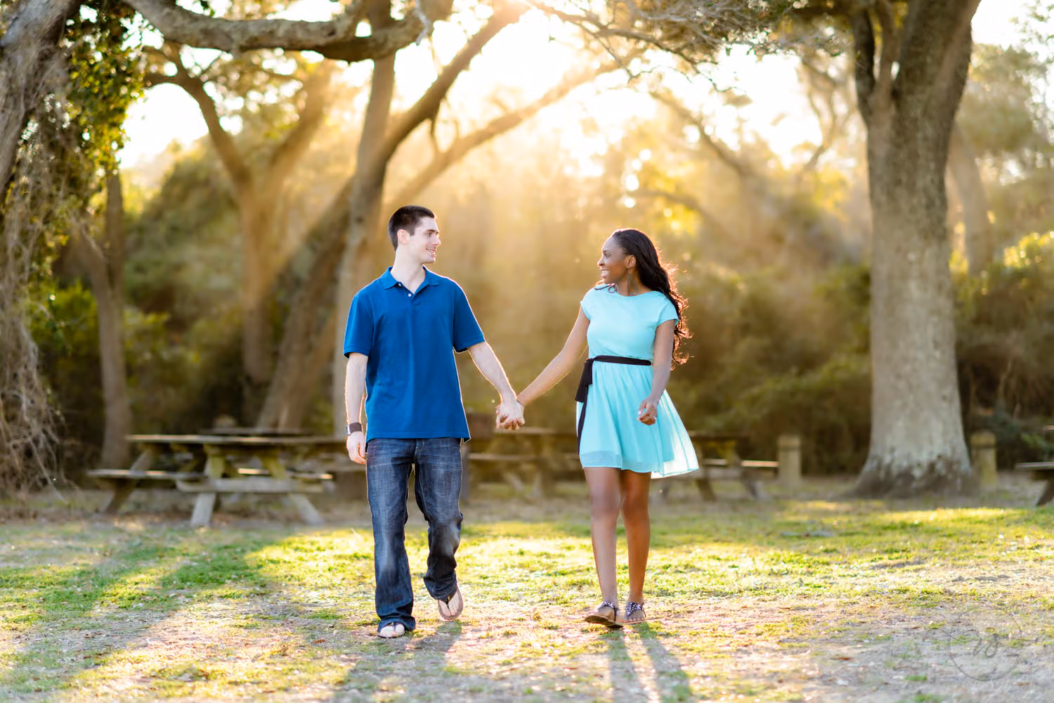 Couple holding hands and walking as sun rays stream through the oak trees behind them at Myrtle Beach State Park