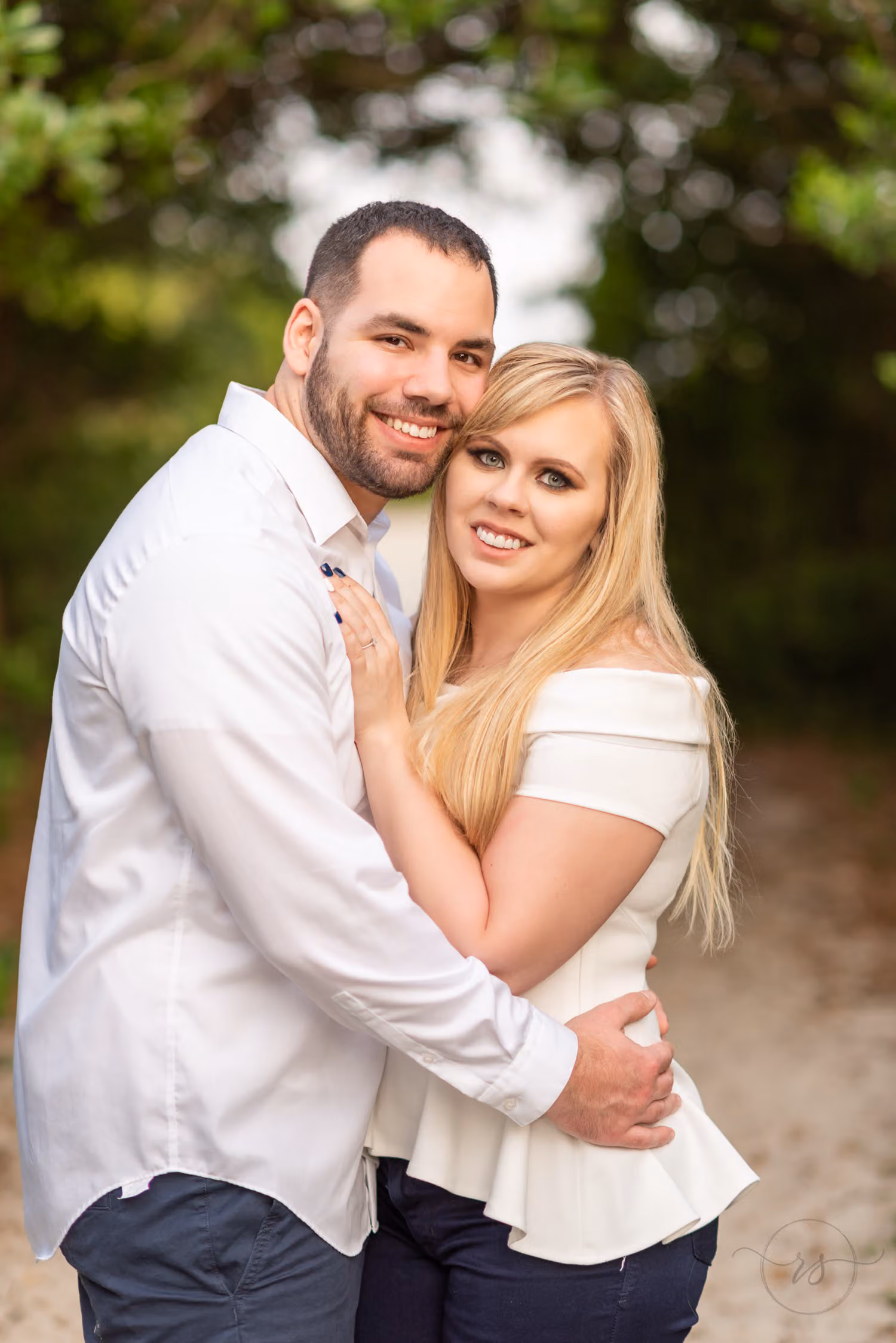 Couple hugging and smiling at the camera on a shaded beach walkway at Huntington Beach State Park