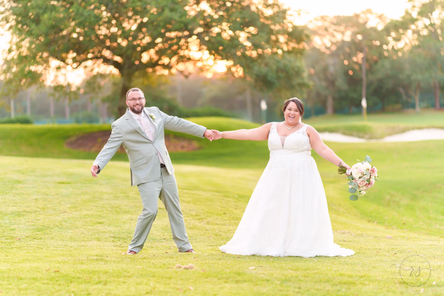 Bride and groom holding hands and laughing as they stretch apart on the golf course at sunset at The Dunes Golf & Beach Club
