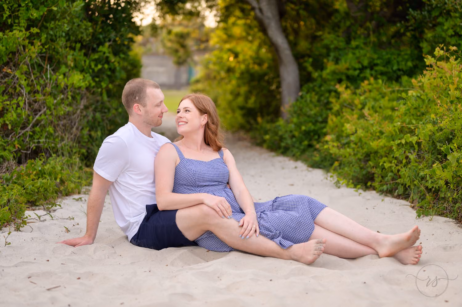 Couple sitting together and smiling at each other on a sandy pathway under the trees at Huntington Beach State Park