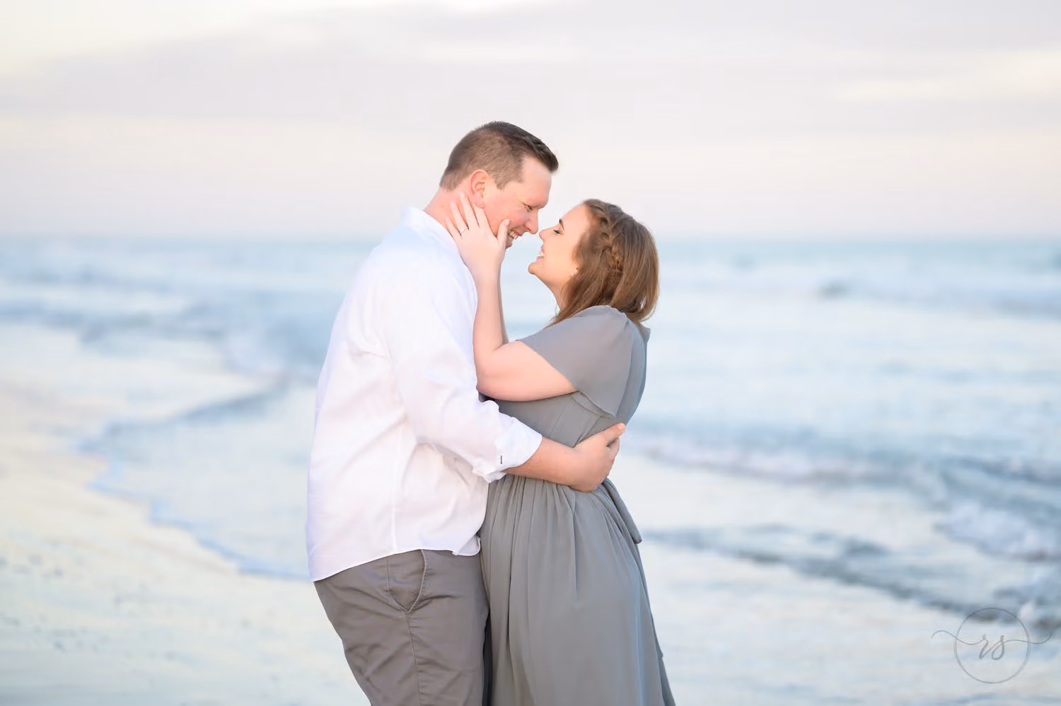 Couple touching noses and smiling with the waves rolling in behind them at Huntington Beach State Park