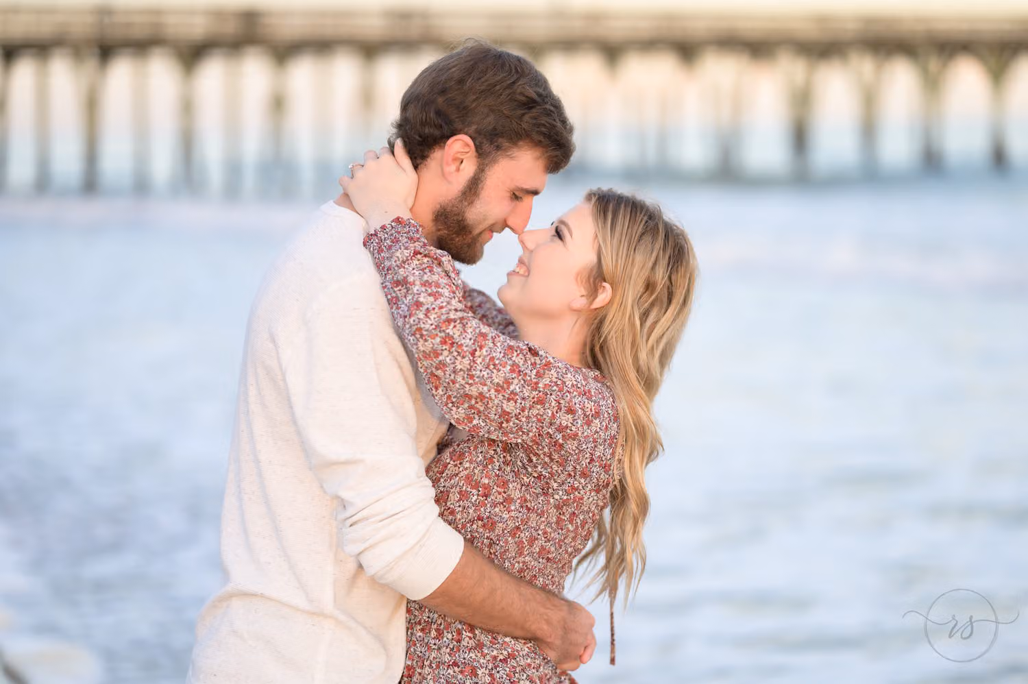 Couple touching noses in a close embrace with the pier softly blurred behind them at Myrtle Beach State Park