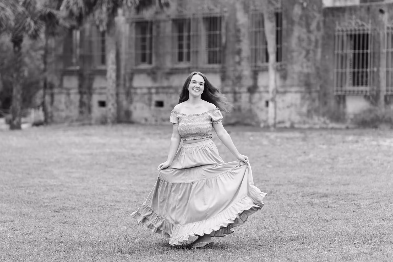 Black and white photo of a senior twirling her long skirt on the lawn by the castle at Huntington Beach State Park