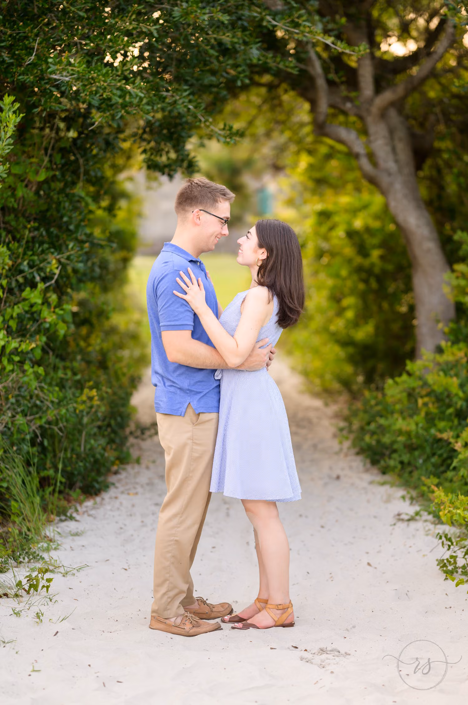 Couple smiling at each other on a sandy path under a canopy of trees at Huntington Beach State Park