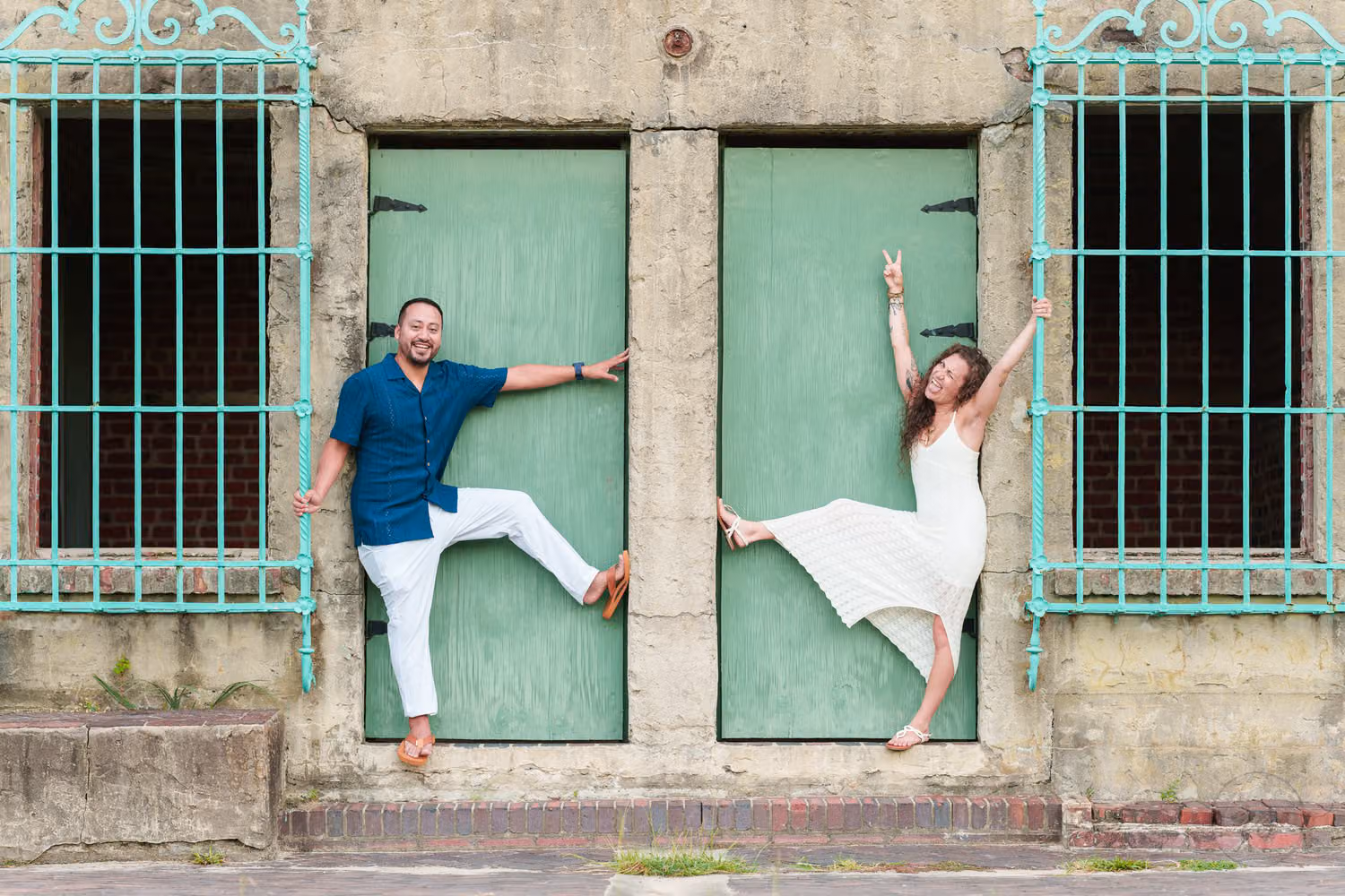 Couple striking playful poses against the green castle doors and turquoise window grates at Huntington Beach State Park