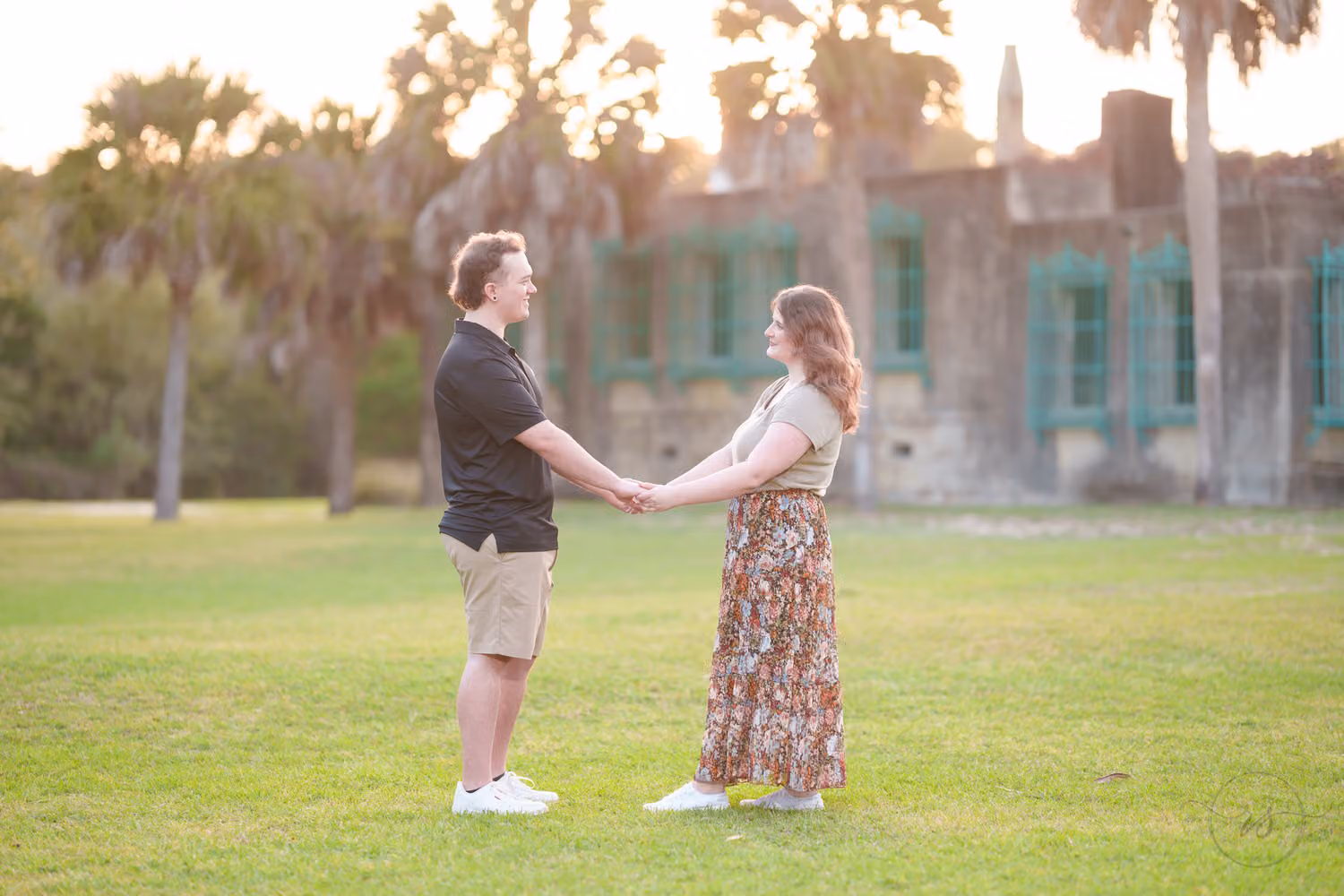Couple holding hands on the lawn in front of the Atalaya castle and palm trees at Huntington Beach State Park
