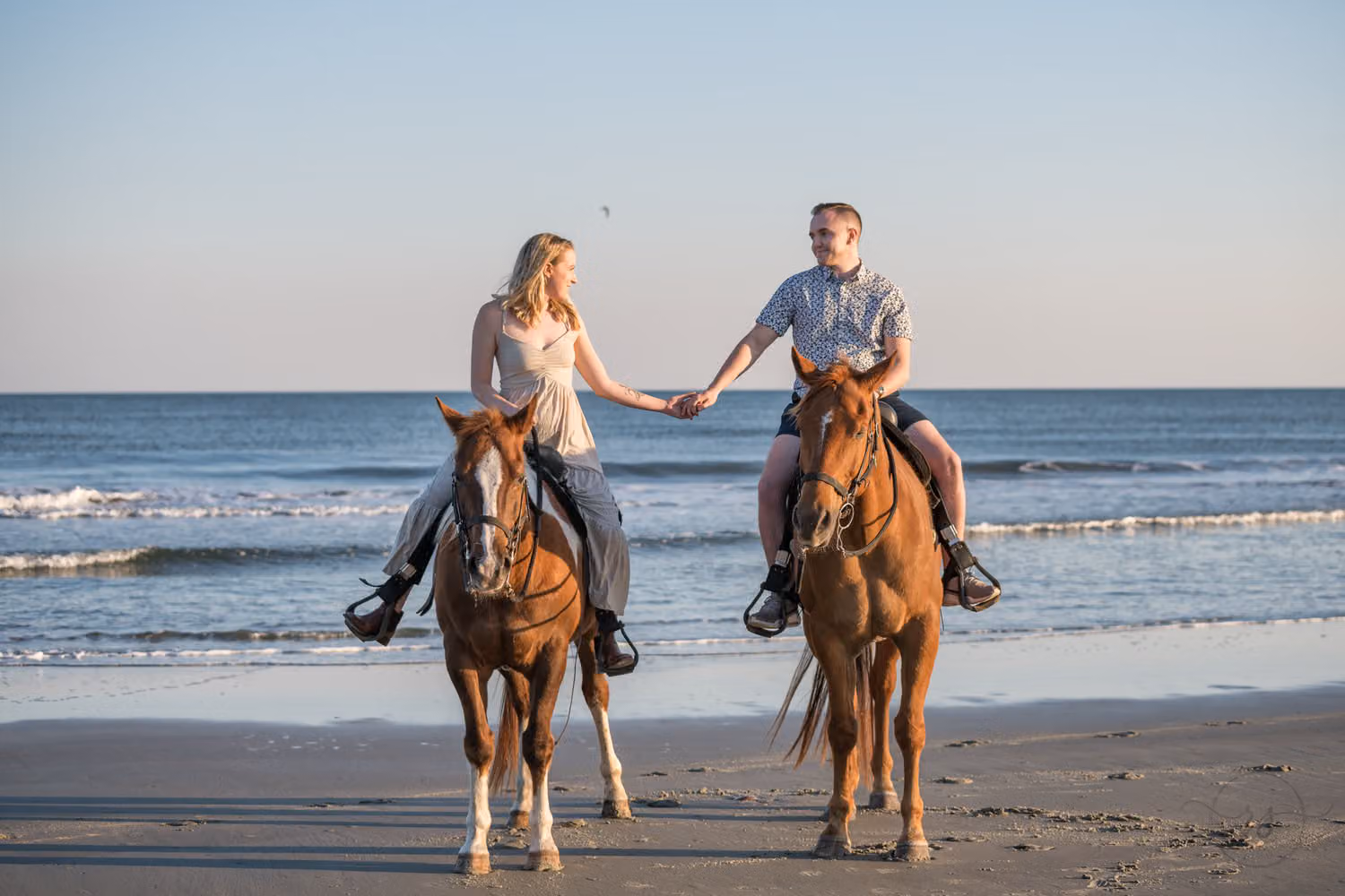 Couple holding hands while riding two horses along the water's edge at Inlet Point Plantation