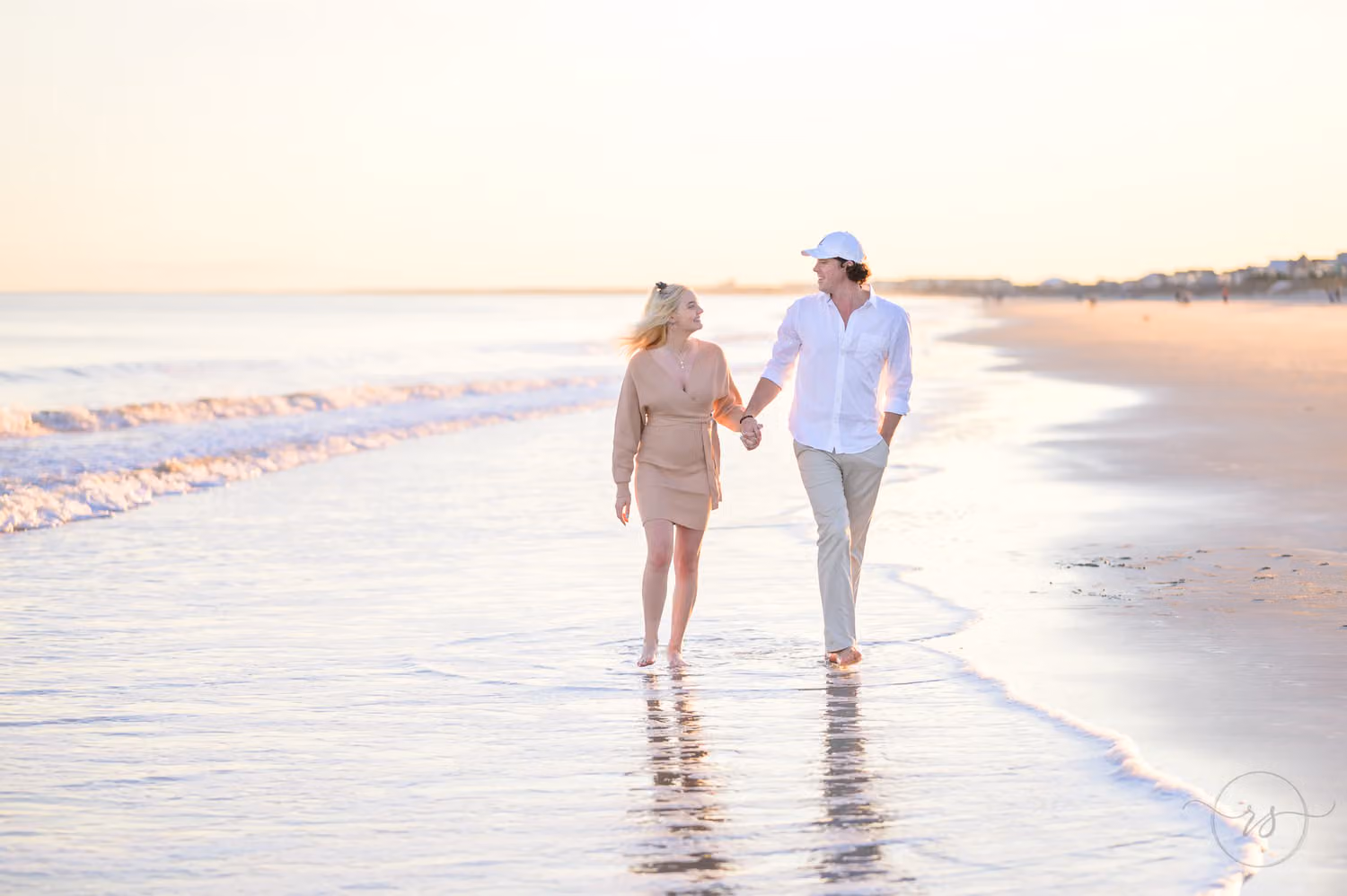 Couple walking hand in hand along the shoreline in warm evening light at Huntington Beach State Park