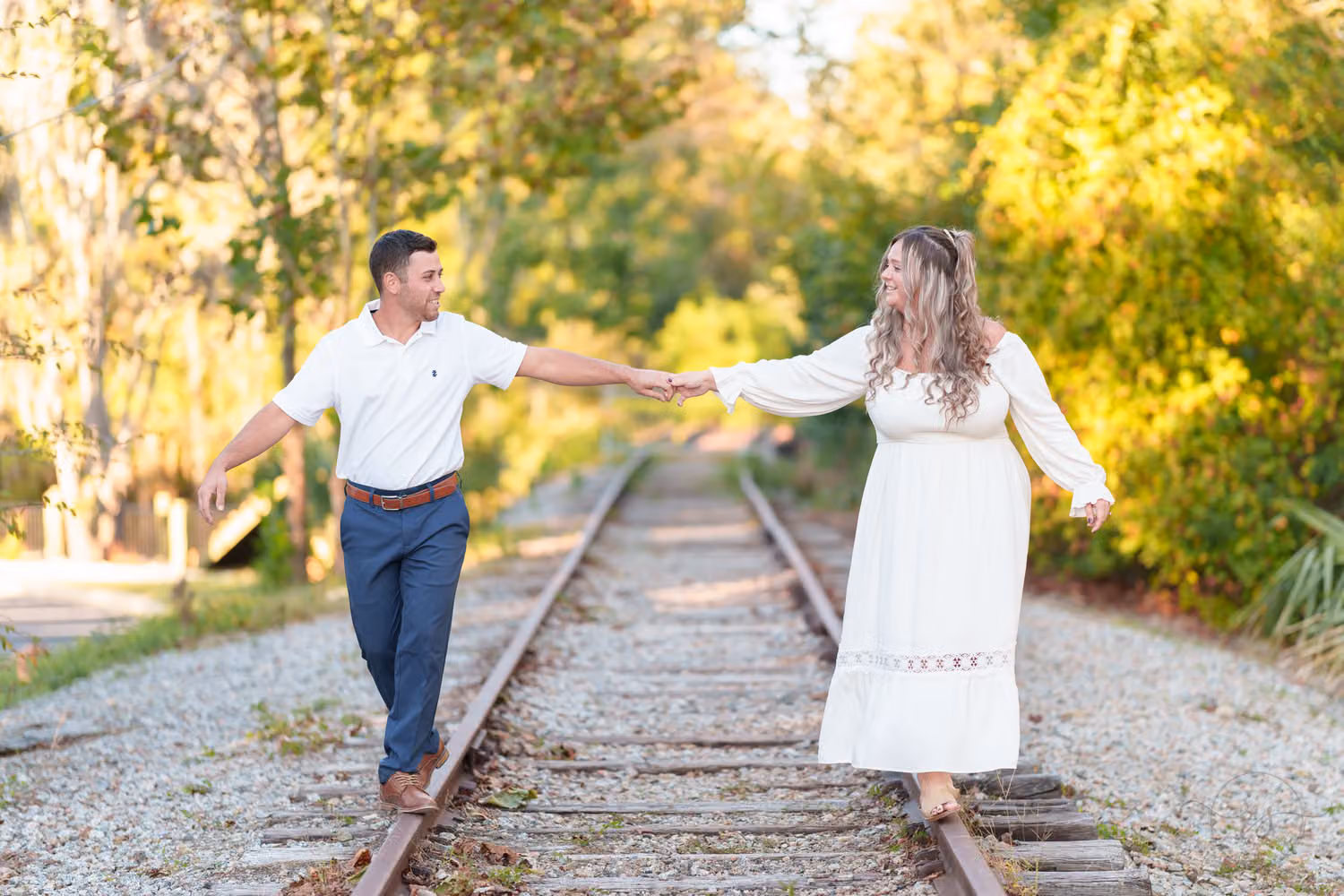 Couple holding hands as they balance on the rails of the train tracks at the Conway Riverwalk