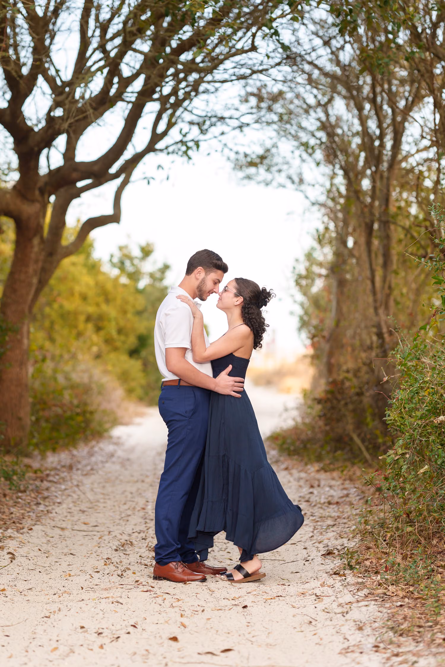 Newly engaged couple about to kiss on a sandy path under arching trees at Huntington Beach State Park