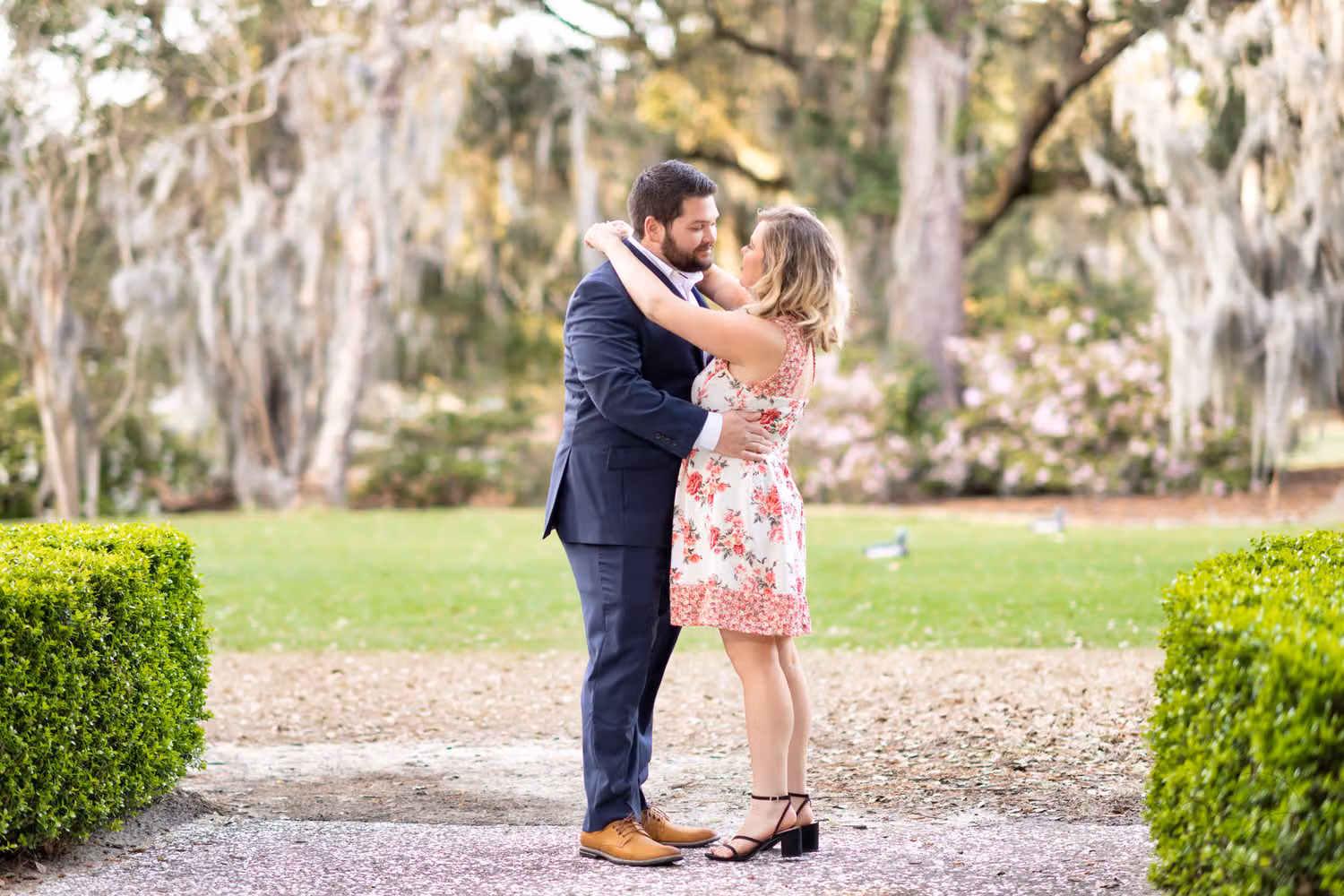 Couple embracing on a path between hedges under mossy oak trees at Caledonia Golf & Fish Club