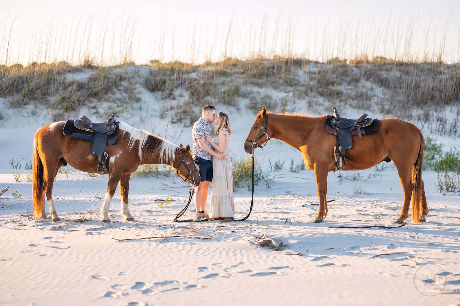 Couple sharing a kiss between their two saddled horses on the beach by the dunes at Inlet Point Plantation
