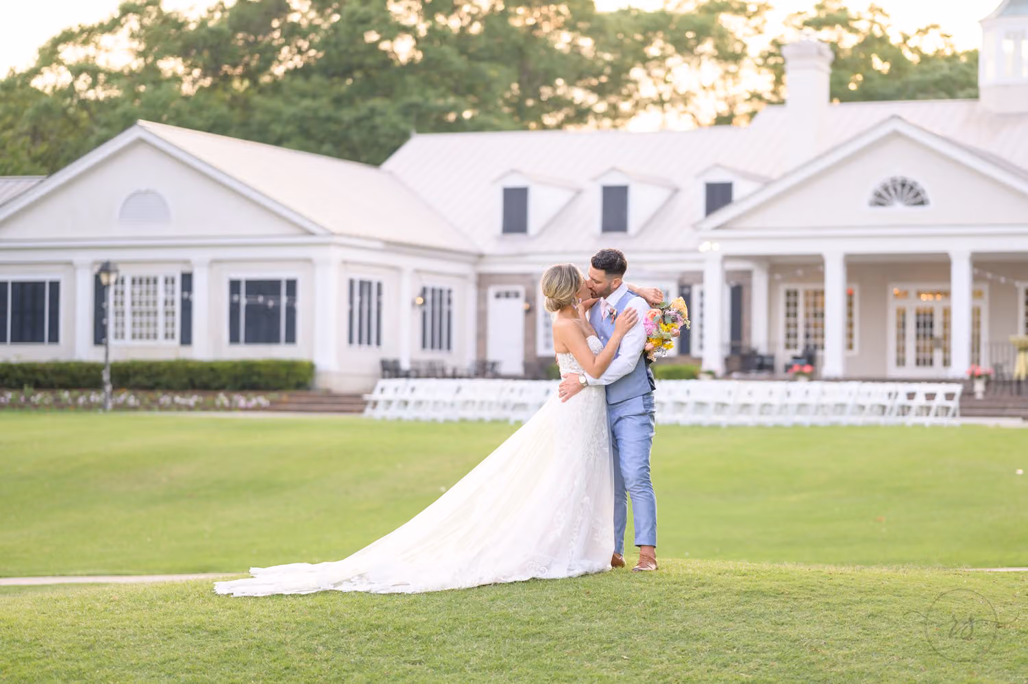 Bride and groom kissing on the lawn with the white clubhouse behind them at Pawleys Plantation Golf & Country Club