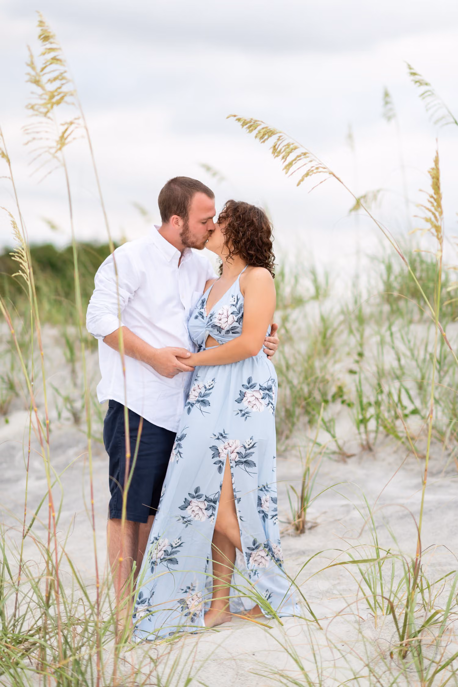 Couple kissing among tall sea oats on the dunes under a cloudy evening sky at Huntington Beach State Park