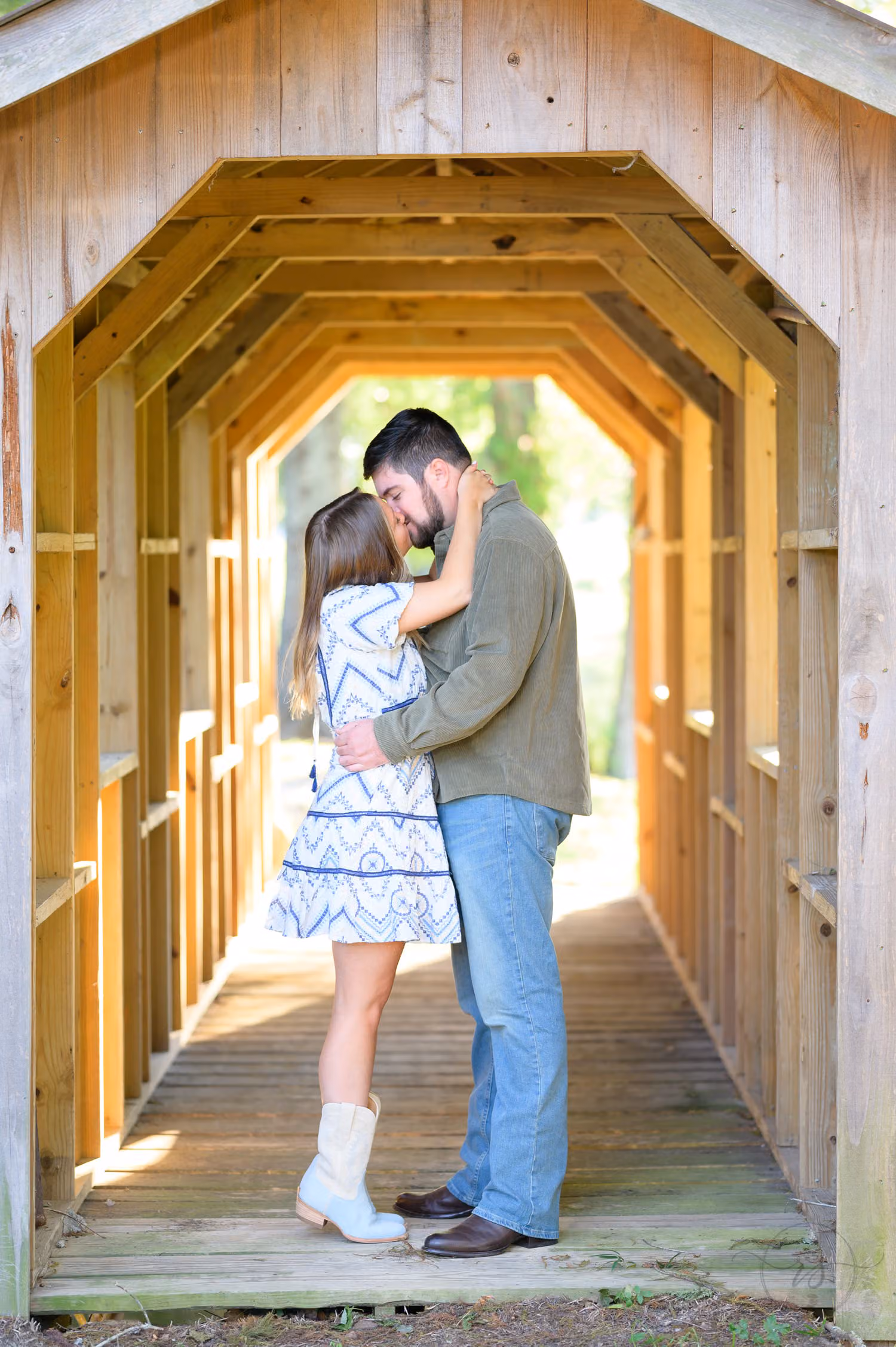 Couple kissing inside a wooden covered bridge with light glowing at the far end at Pine Log Plantation