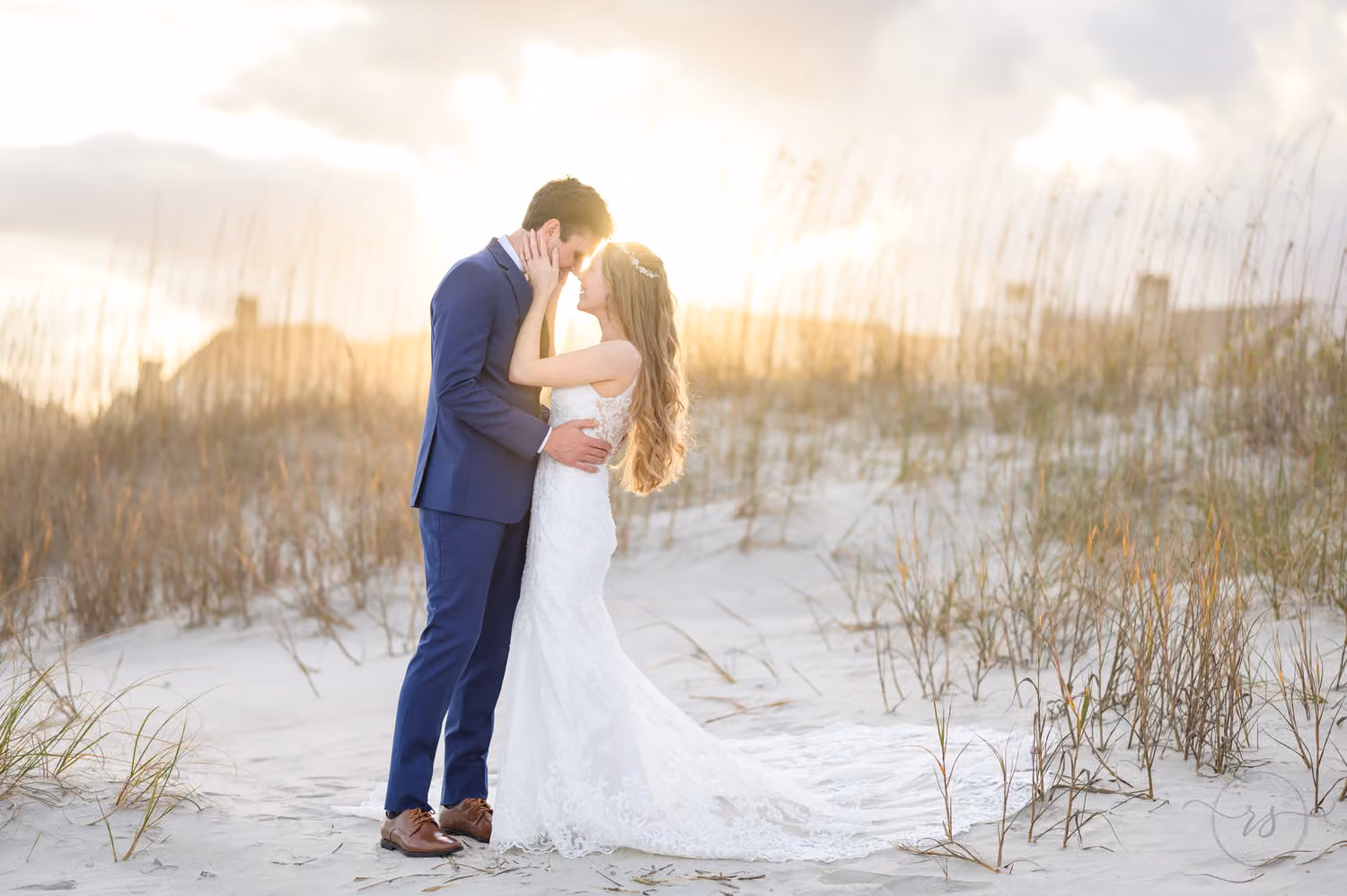 Bride and groom kissing among the sea oats on the dunes with the sun glowing behind them in Pawleys Island