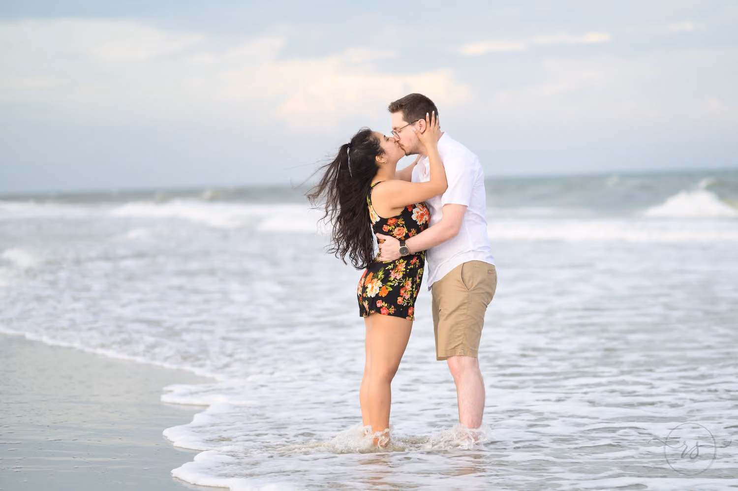 Couple kissing as they stand in the shallow waves at the edge of the ocean at Huntington Beach State Park