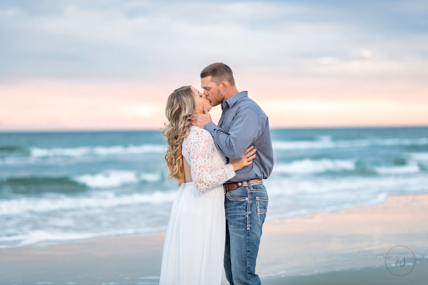 Couple kissing at the water's edge under a pink and blue evening sky at Huntington Beach State Park