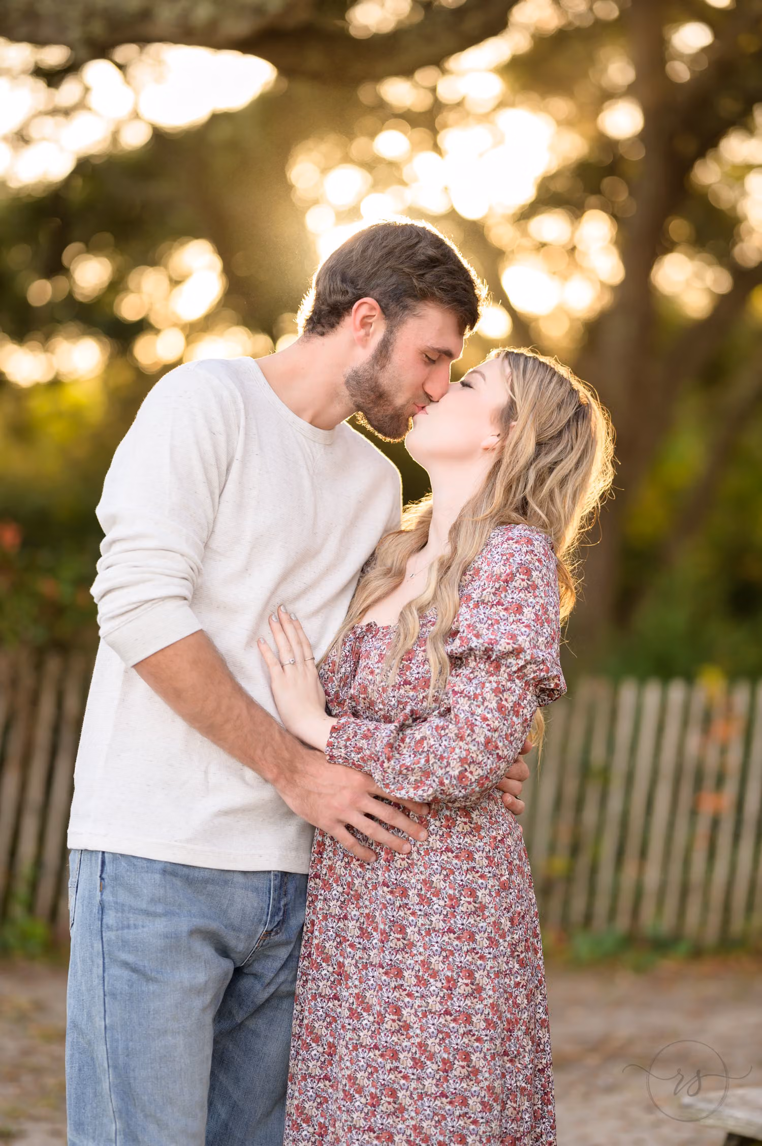 Couple kissing by a wooden fence with sunlight filtering through the trees at Myrtle Beach State Park