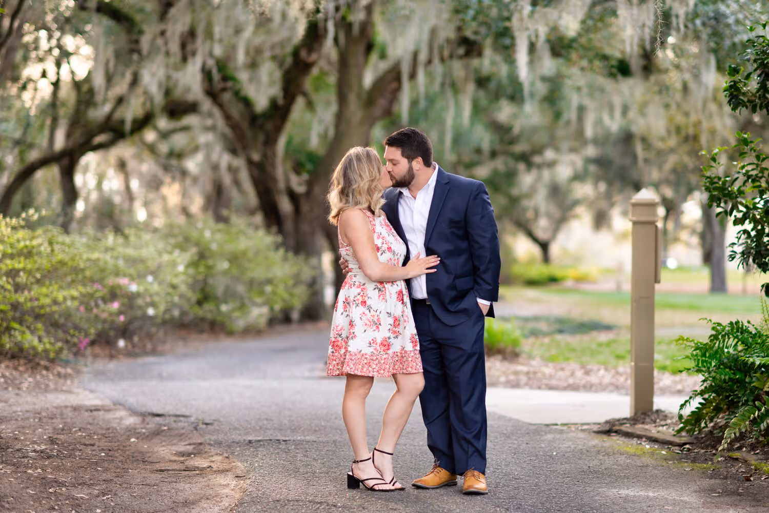 Couple kissing on a paved path shaded by oaks with Spanish moss at Caledonia Golf & Fish Club