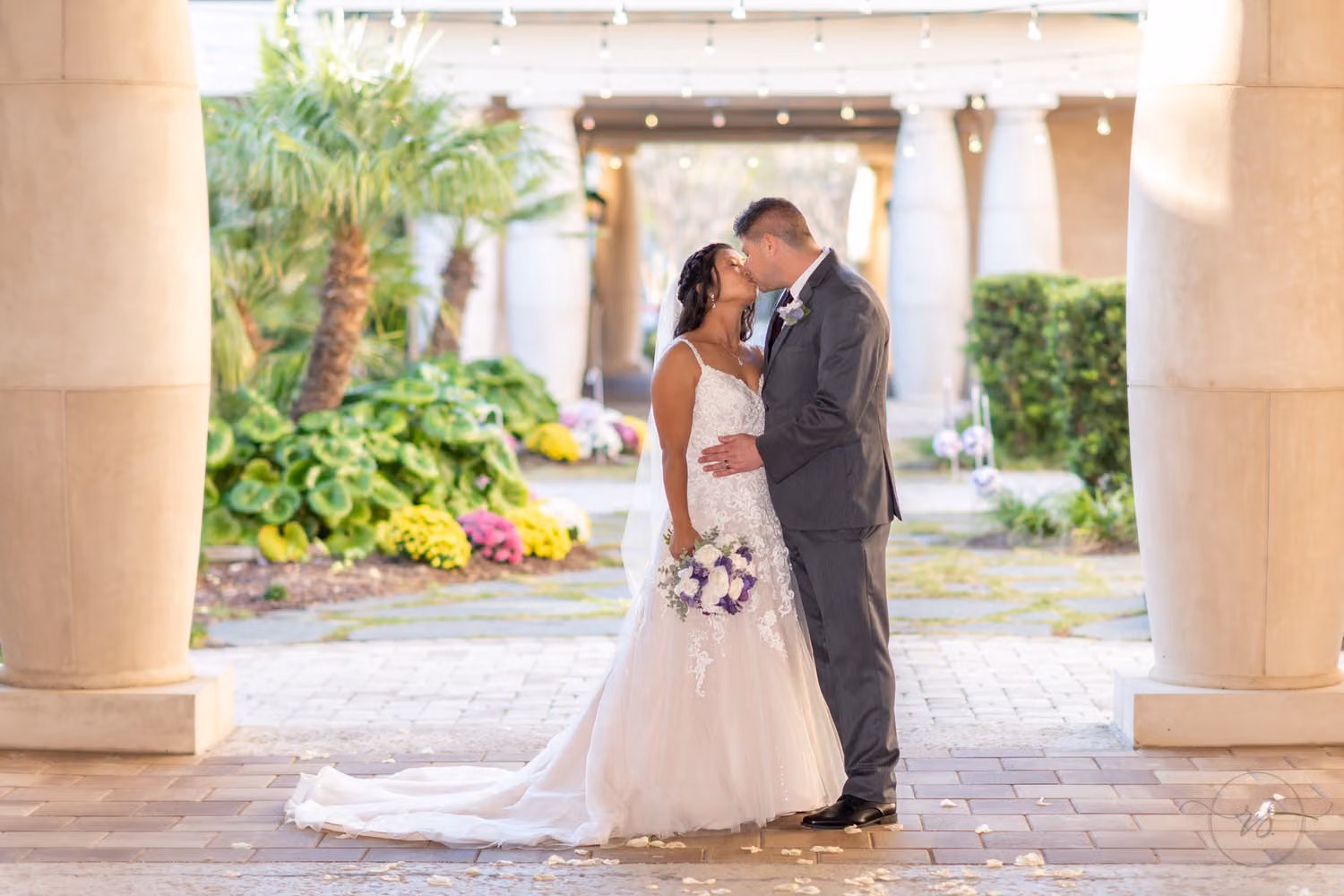 Bride with a purple bouquet kissing the groom in gray between the courtyard columns at 21 Main Events at North Beach
