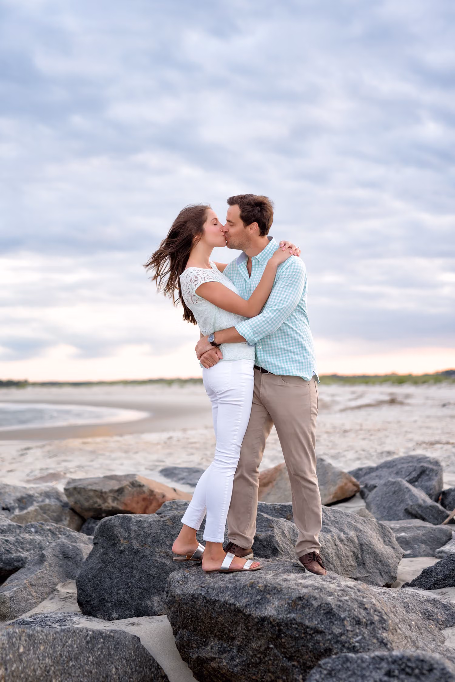 Couple kissing on the rocks of the jetty under a soft cloudy sky in Murrells Inlet