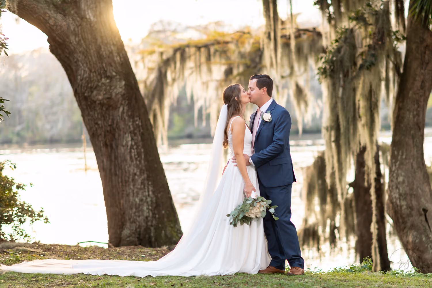 Bride and groom kissing between moss-draped oaks with the Waccamaw River behind them at Kimbel's at Wachesaw Plantation