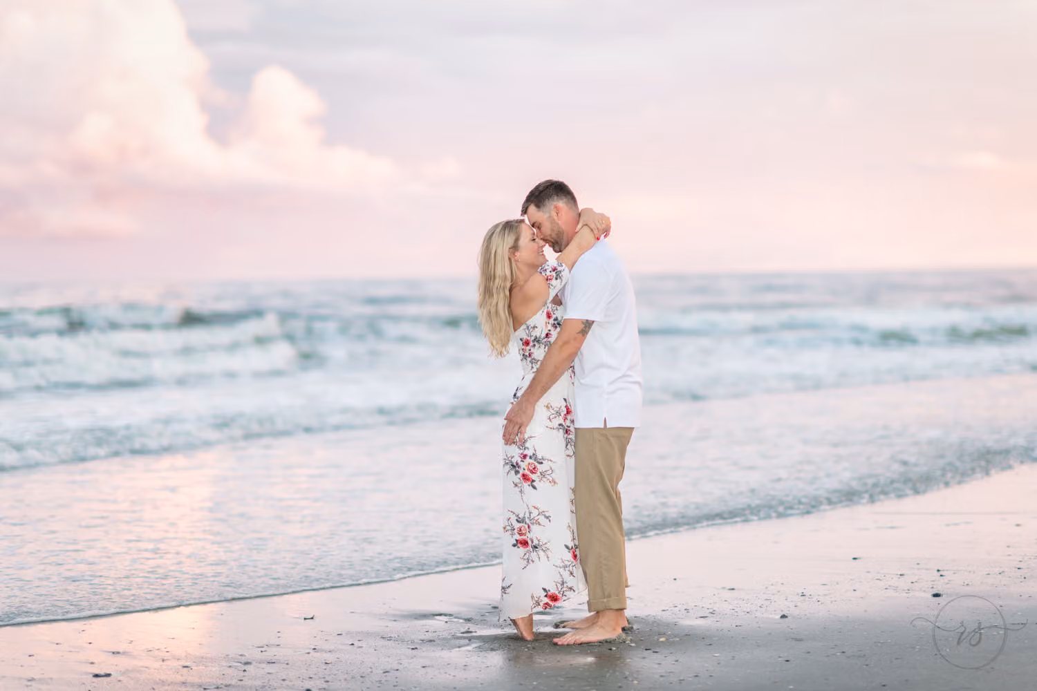 Couple kissing at the water's edge under soft pink clouds after the rain at Grande Dunes Ocean Club