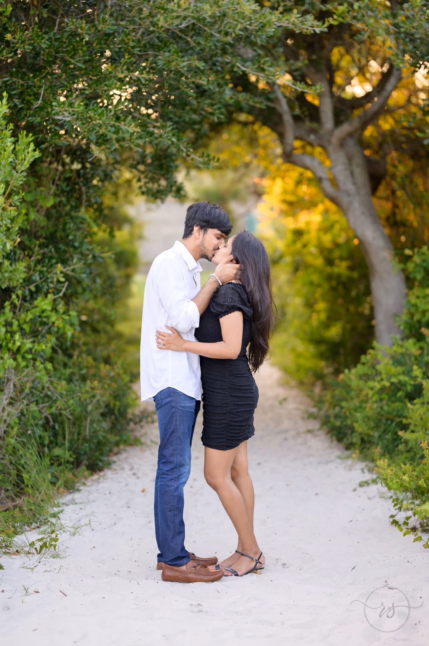 Couple about to kiss on a sandy path beneath arching trees on the way to the castle at Huntington Beach State Park
