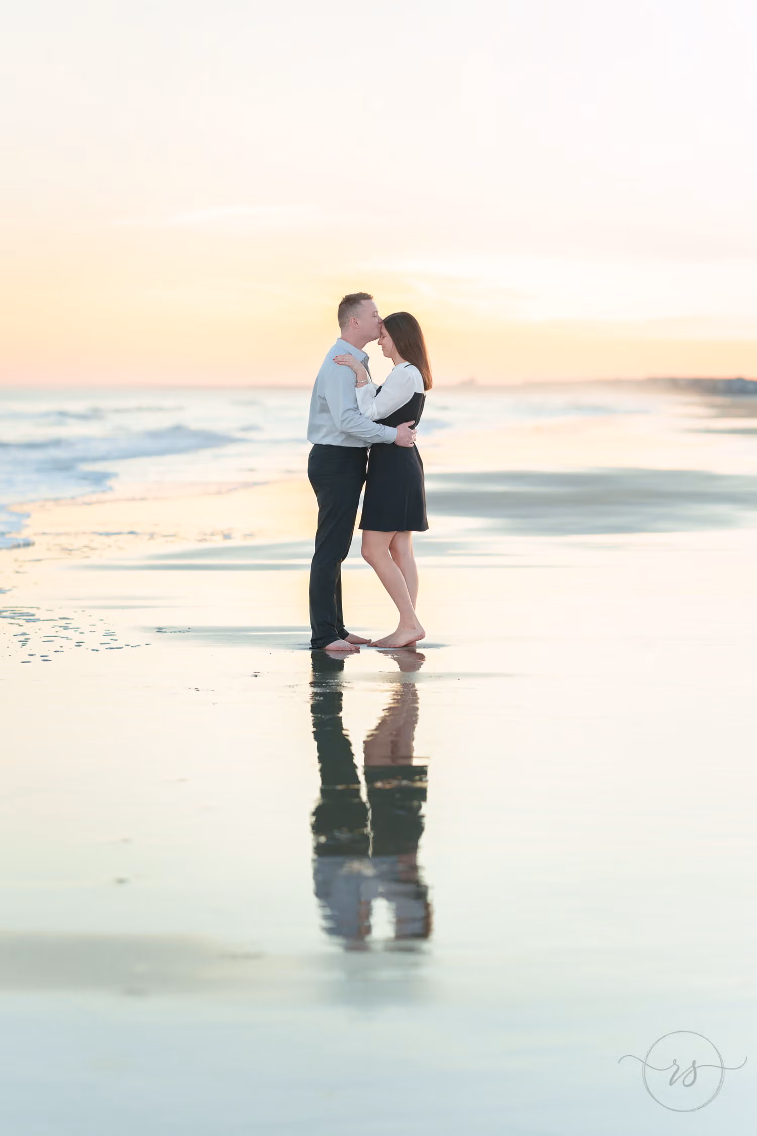 Couple kissing at the water's edge with their reflection on the wet sand at sunset at Huntington Beach State Park