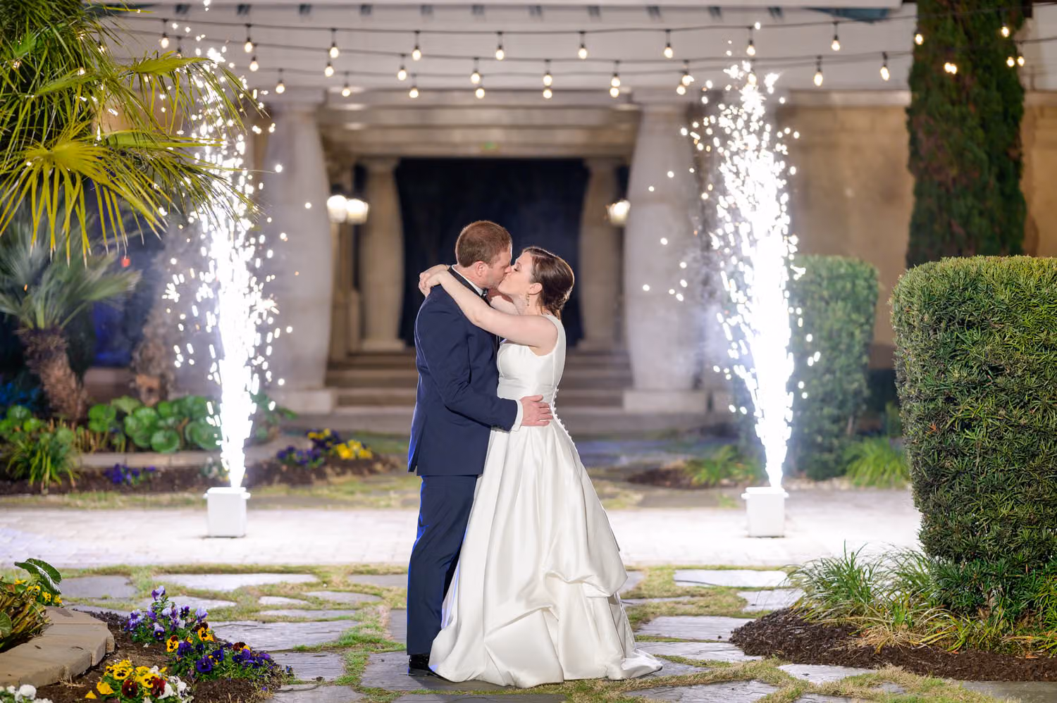 Bride and groom kissing between two cold spark fountains on the courtyard path at night at 21 Main Events at North Beach