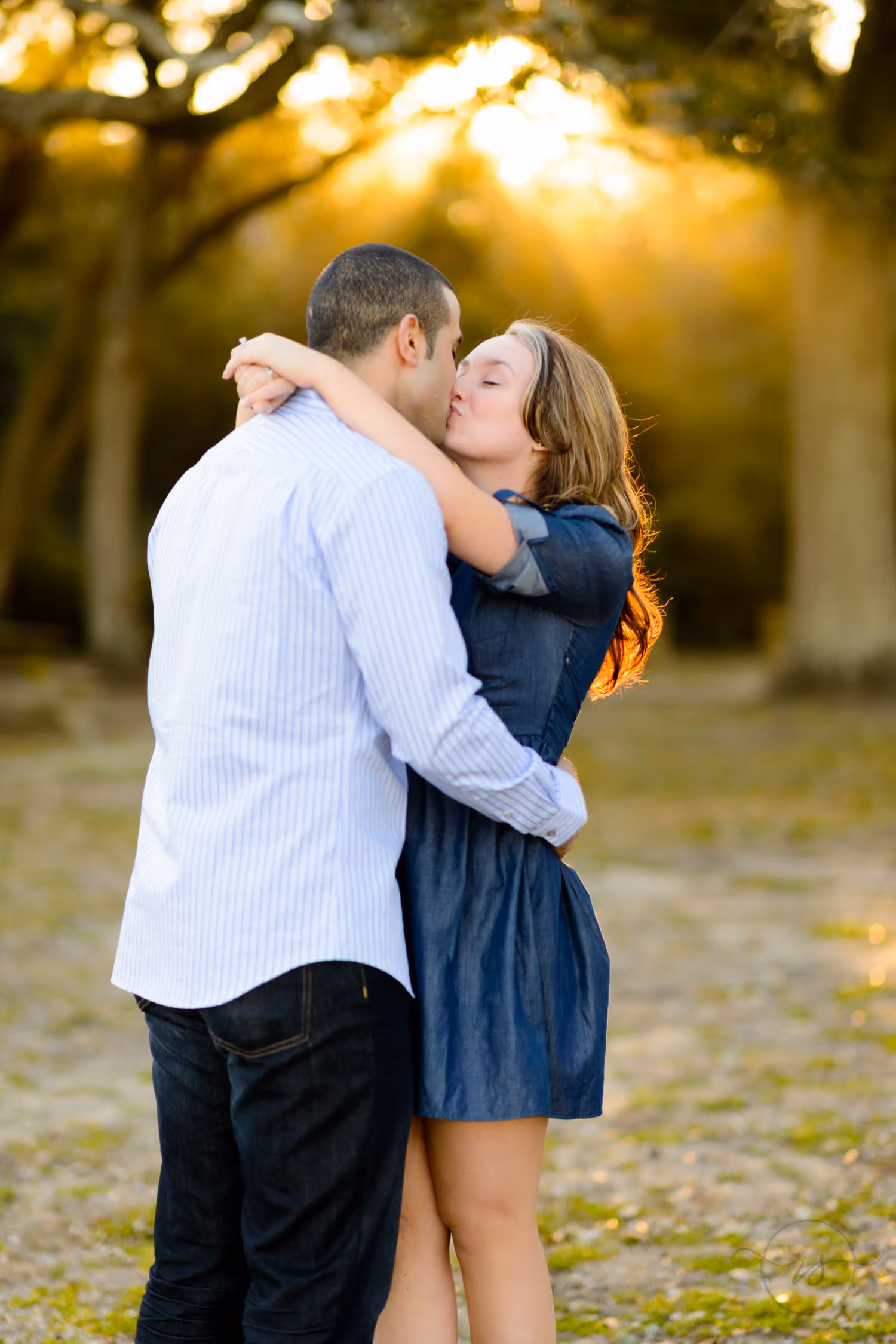 Couple kissing with arms wrapped around each other as bright sunlight glows through the trees at Myrtle Beach State Park