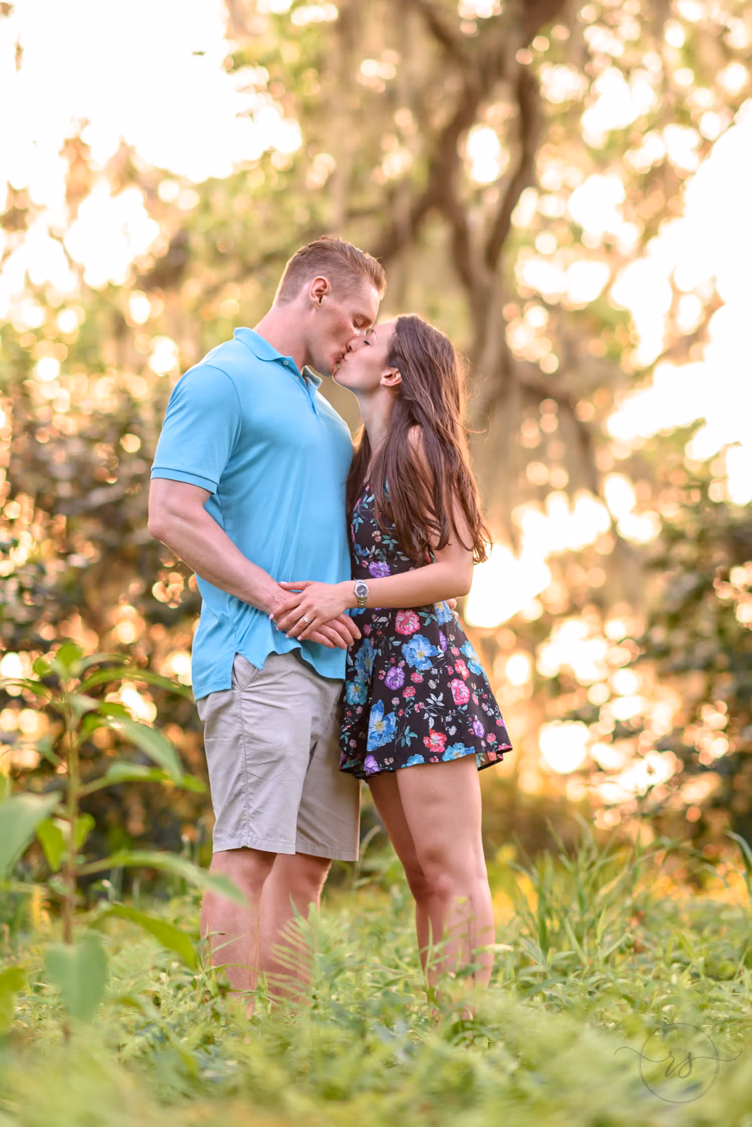 Couple kissing in tall grass with warm sunlight filtering through the trees at Brookgreen Gardens