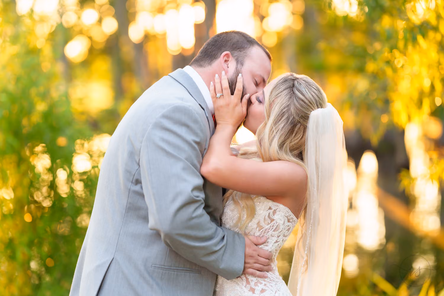 Groom cradling the bride's face for a kiss with golden sunset light glowing through the trees at Wildhorse at Parker Farms