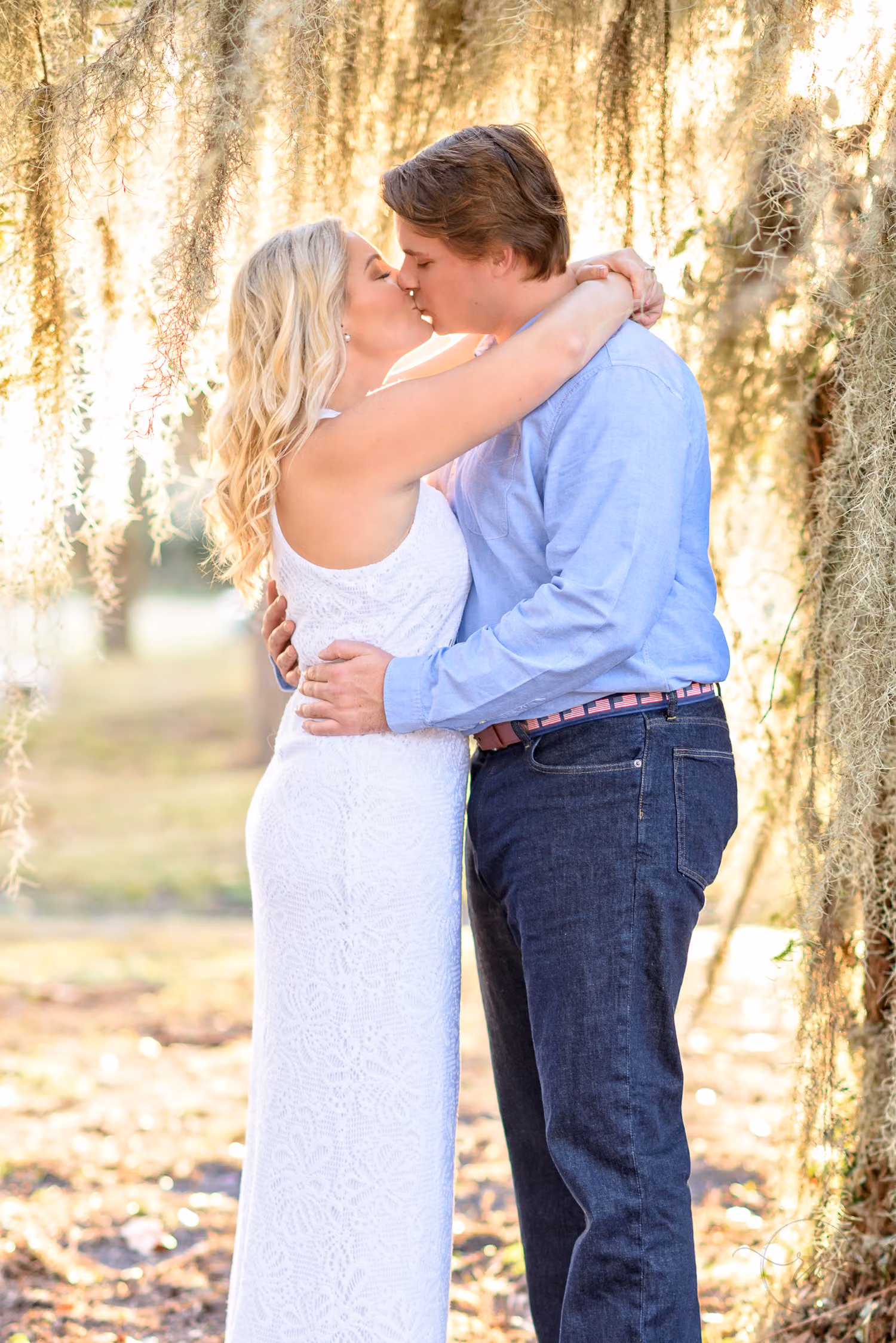 Couple kissing as sunlight glows through hanging Spanish moss around them at Litchfield Plantation