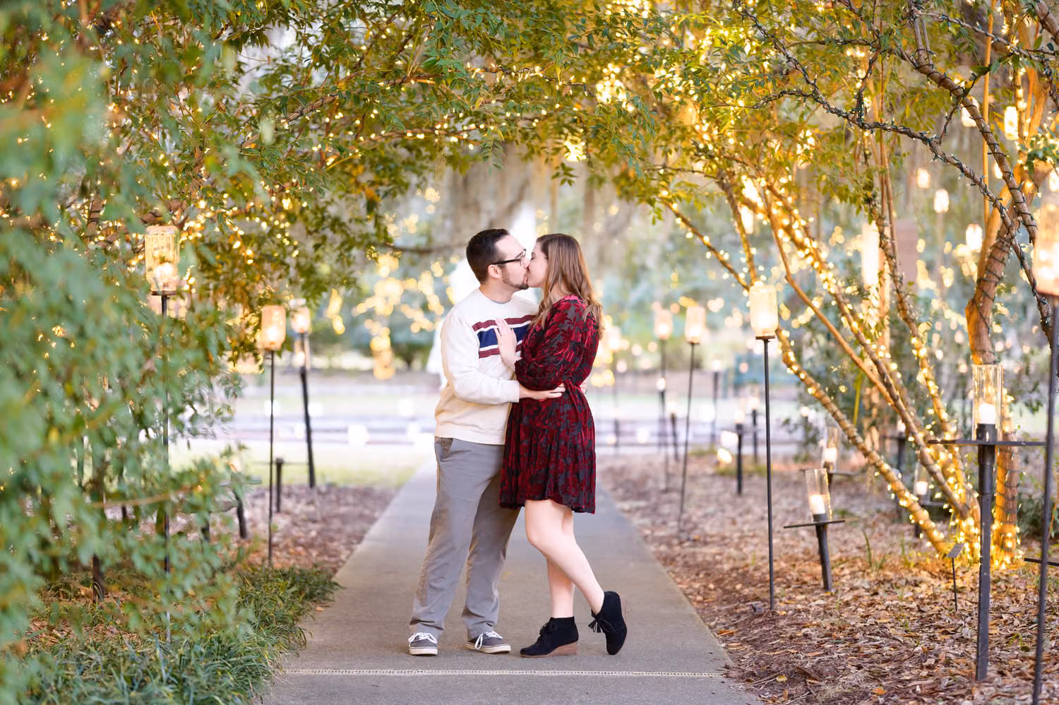 Couple kissing on a garden walkway lined with lanterns under a canopy of glowing lights at Brookgreen Gardens