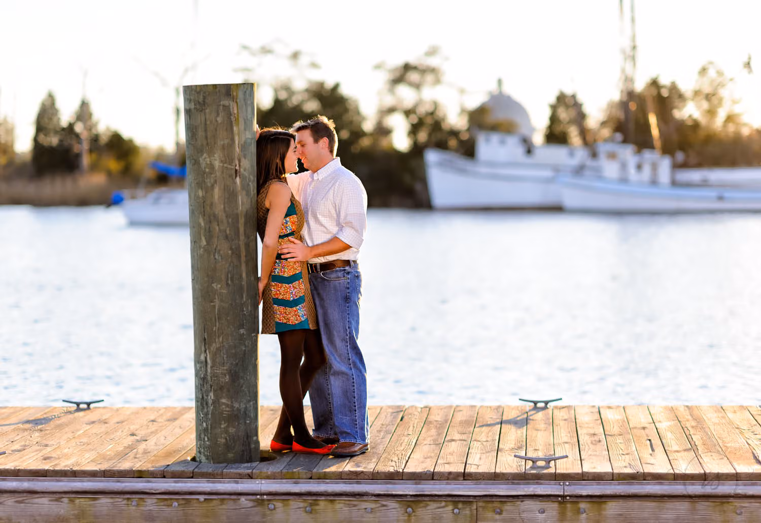Couple kissing beside a wooden piling on a dock with shrimp boats on the water in Downtown Georgetown