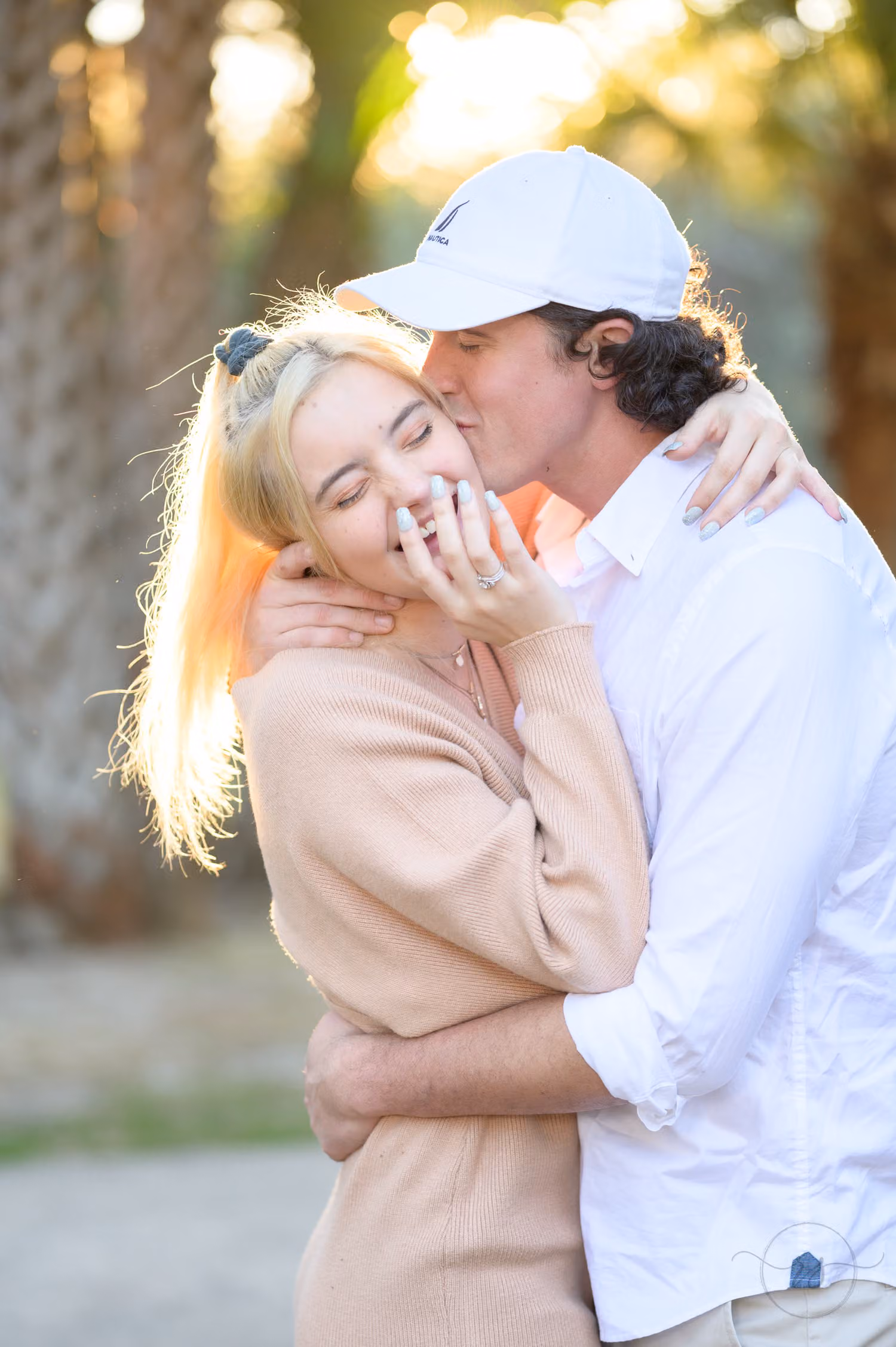 Woman laughing with her eyes closed as her fiancé in a white cap kisses her cheek at Huntington Beach State Park
