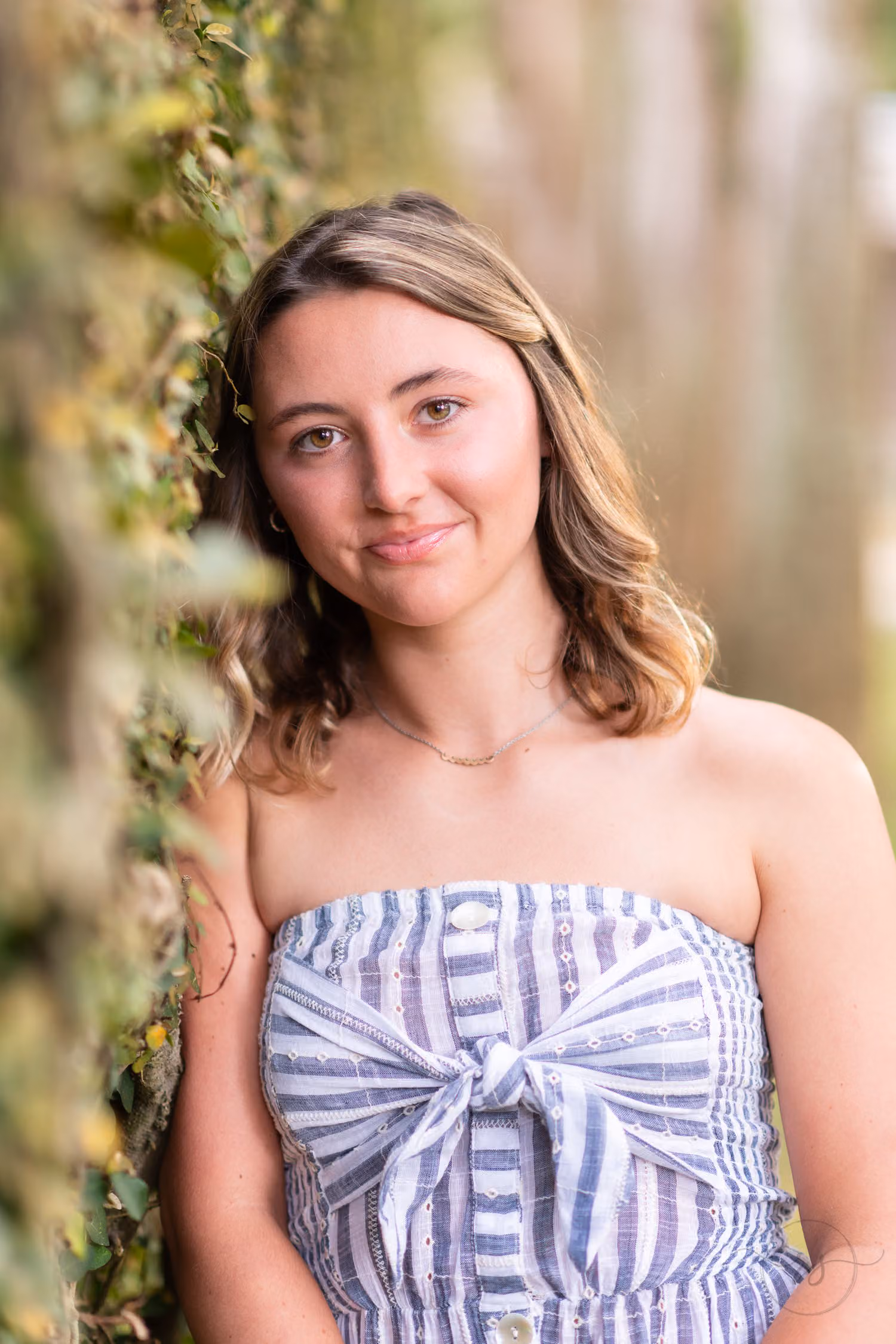 Close-up of a senior in a striped strapless top leaning against the ivy wall at Huntington Beach State Park