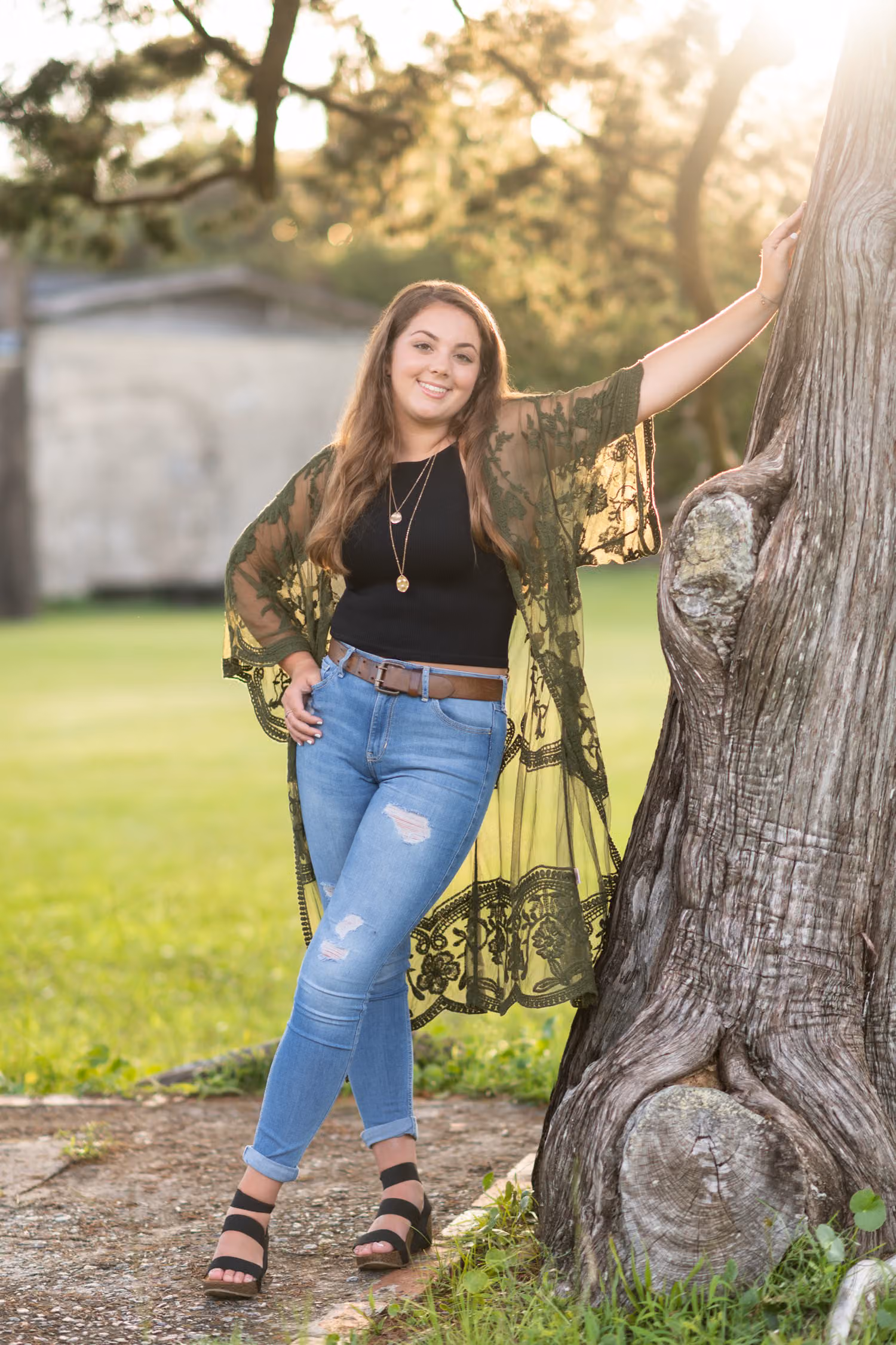 Senior in jeans and a lace kimono leaning on a gnarled old tree trunk at Atalaya Castle